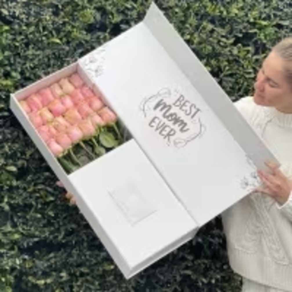 Box of pink tulips held by a person outdoors