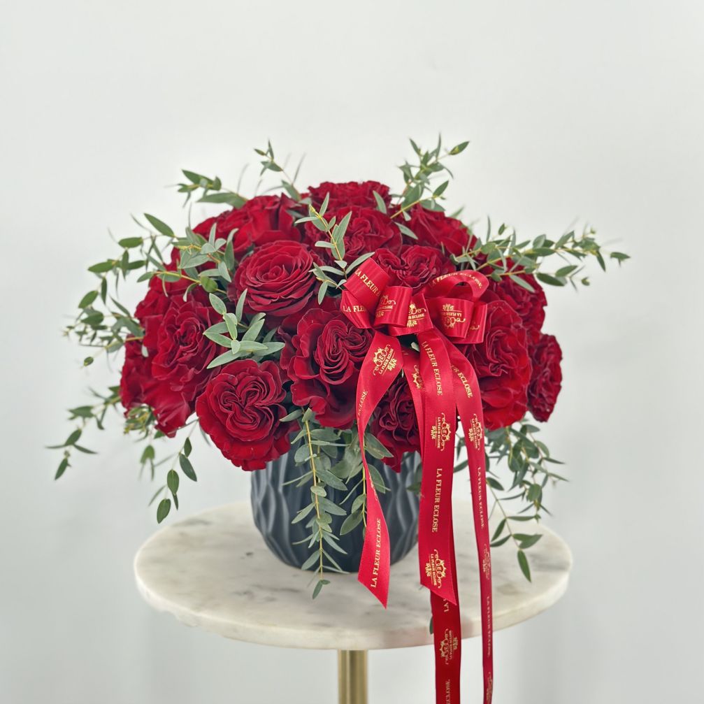 Red rose arrangement in a dark vase with a red ribbon