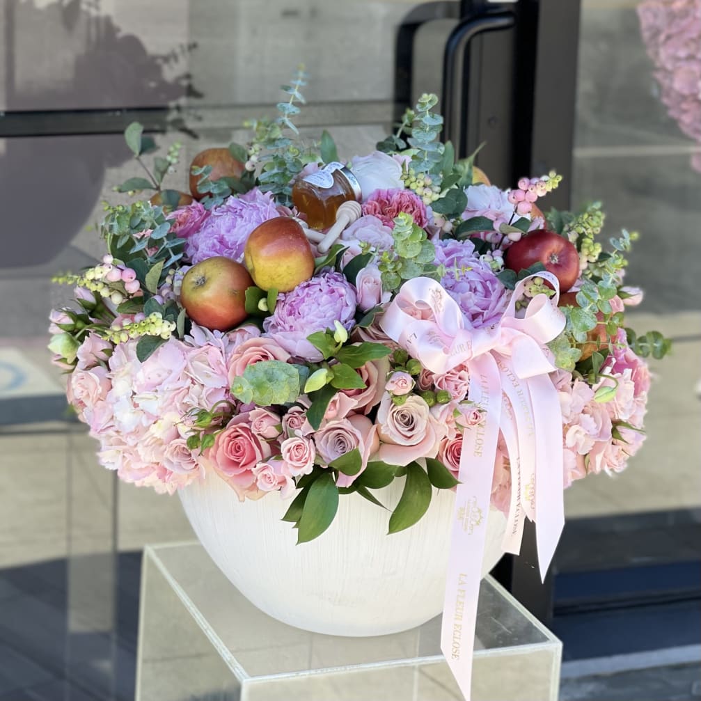 Pink floral arrangement in a white vase with apples and a ribbon bow