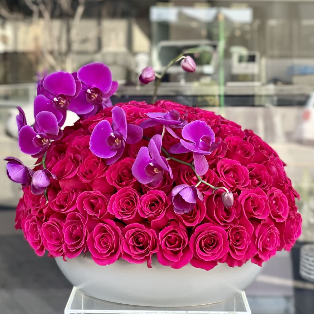 Hot pink roses with purple orchids in a white bowl vase