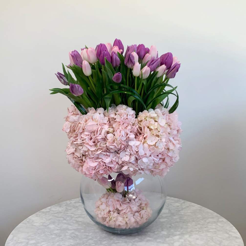Pink hydrangeas and purple tulips arranged in a clear glass vase