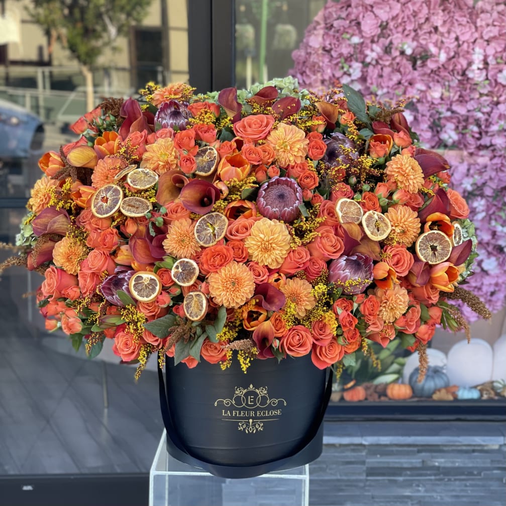 Large orange floral arrangement in a black hatbox with dried citrus slices