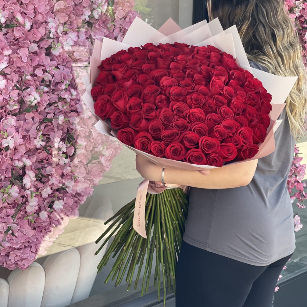 Woman holding a large bouquet of red roses wrapped in pale pink paper