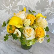 Yellow and white roses with yellow calla lilies in a glass vase