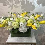 Yellow calla lilies and white flowers arranged in a green rectangular vase