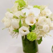 White floral arrangement in a glass vase with green accents