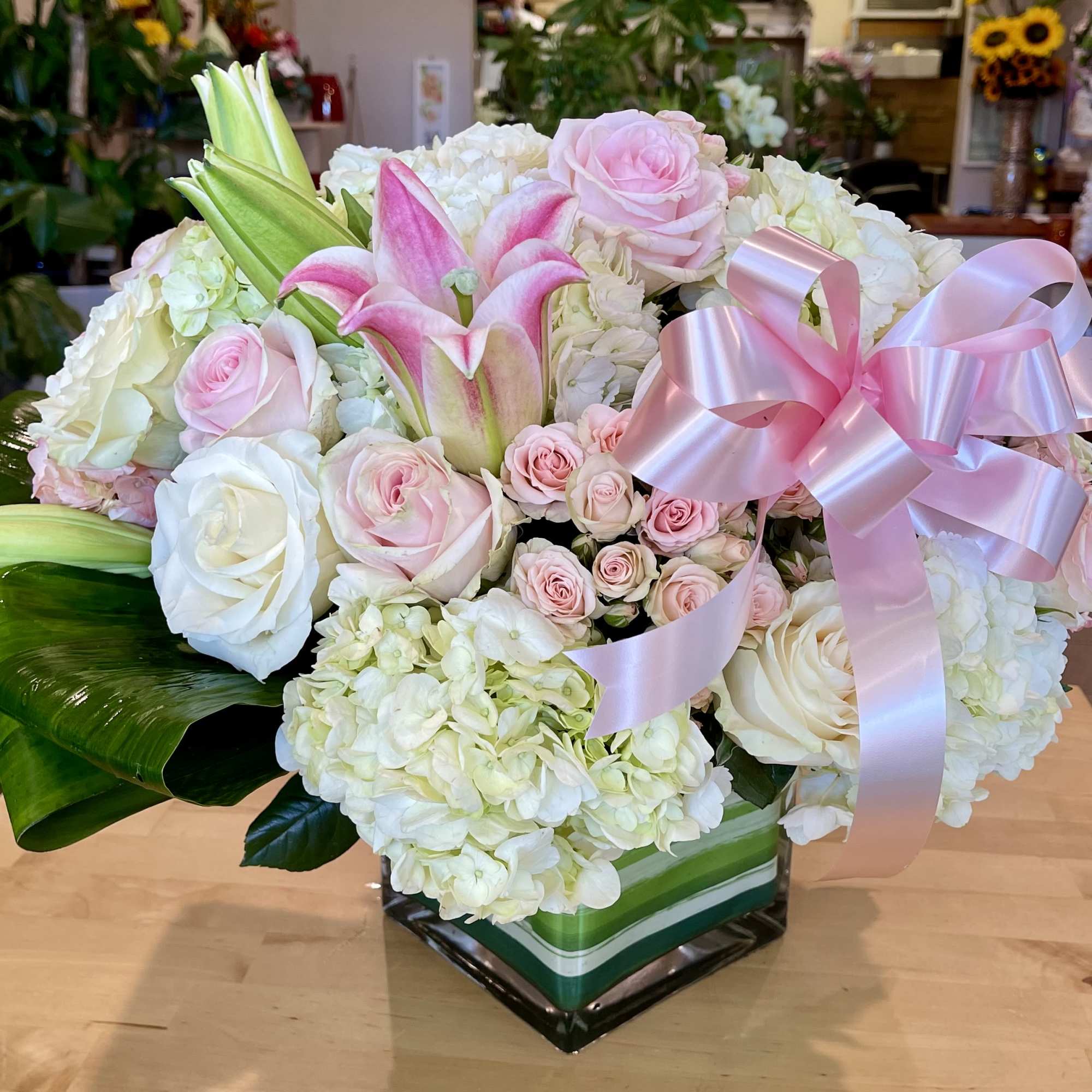 Pink and white floral arrangement with lilies, roses, and hydrangeas in a square vase