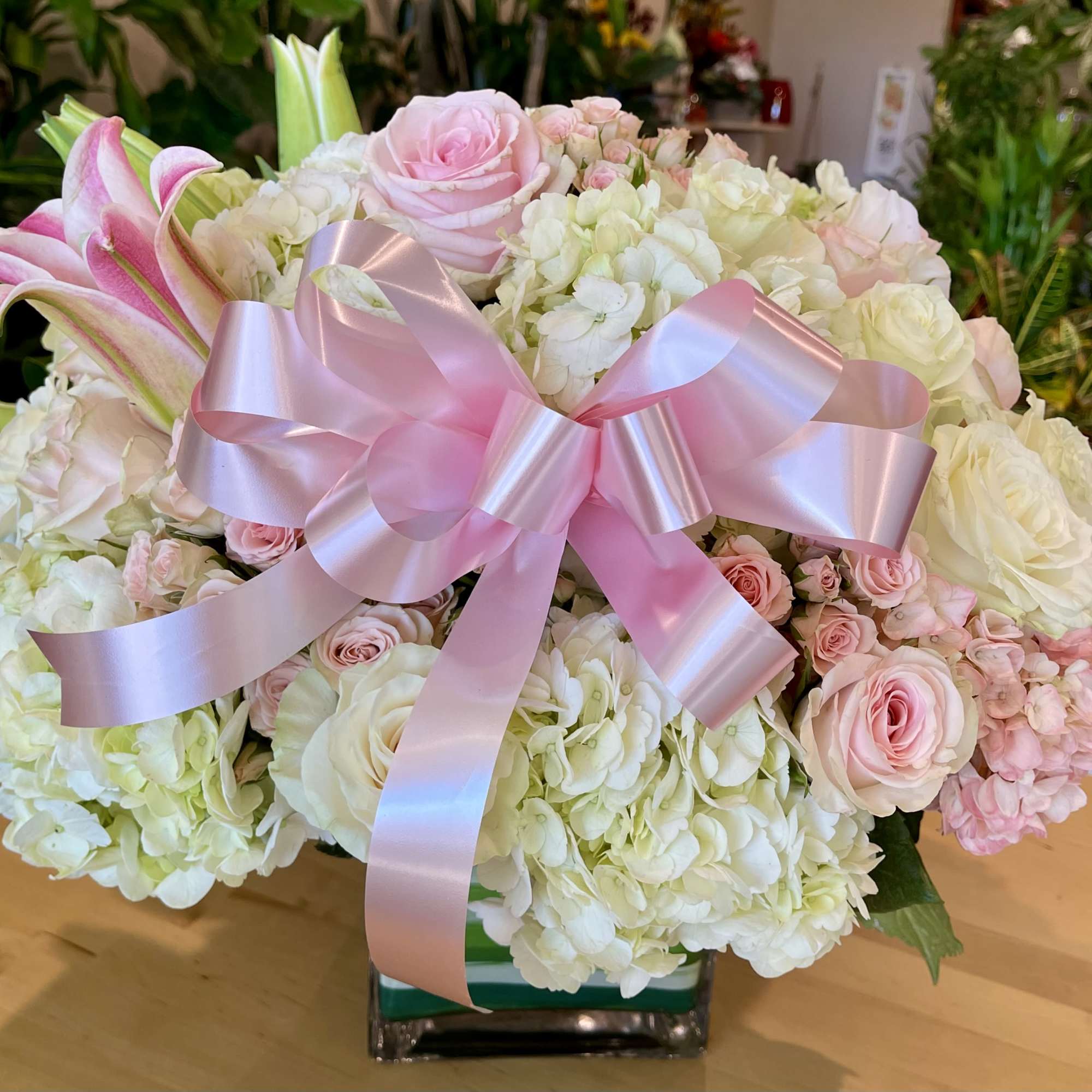 Pink and white floral arrangement with a large pink ribbon in a square vase