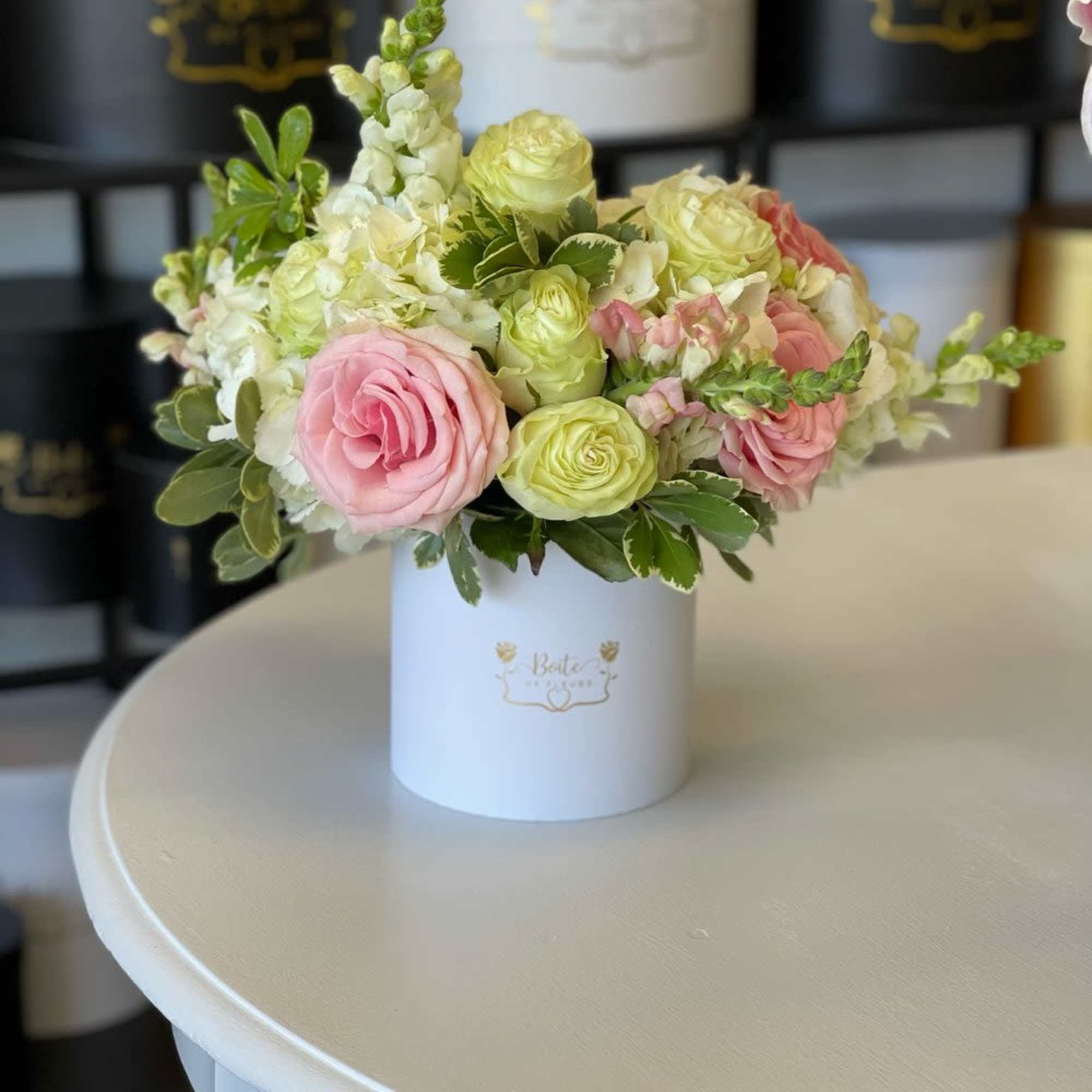 Pink and pale green flowers arranged in a white hat box
