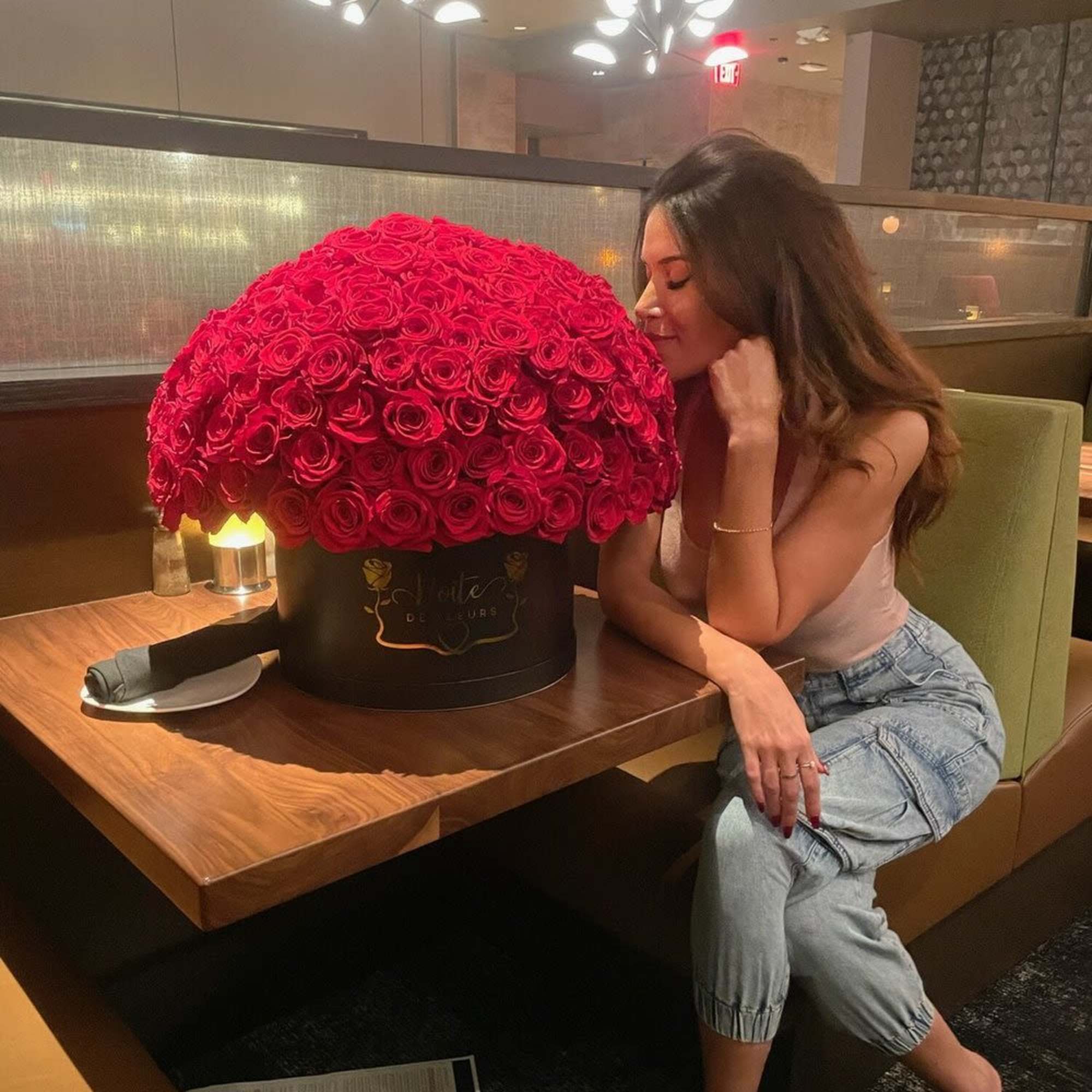 Large dome of red roses in a black hatbox beside a seated woman