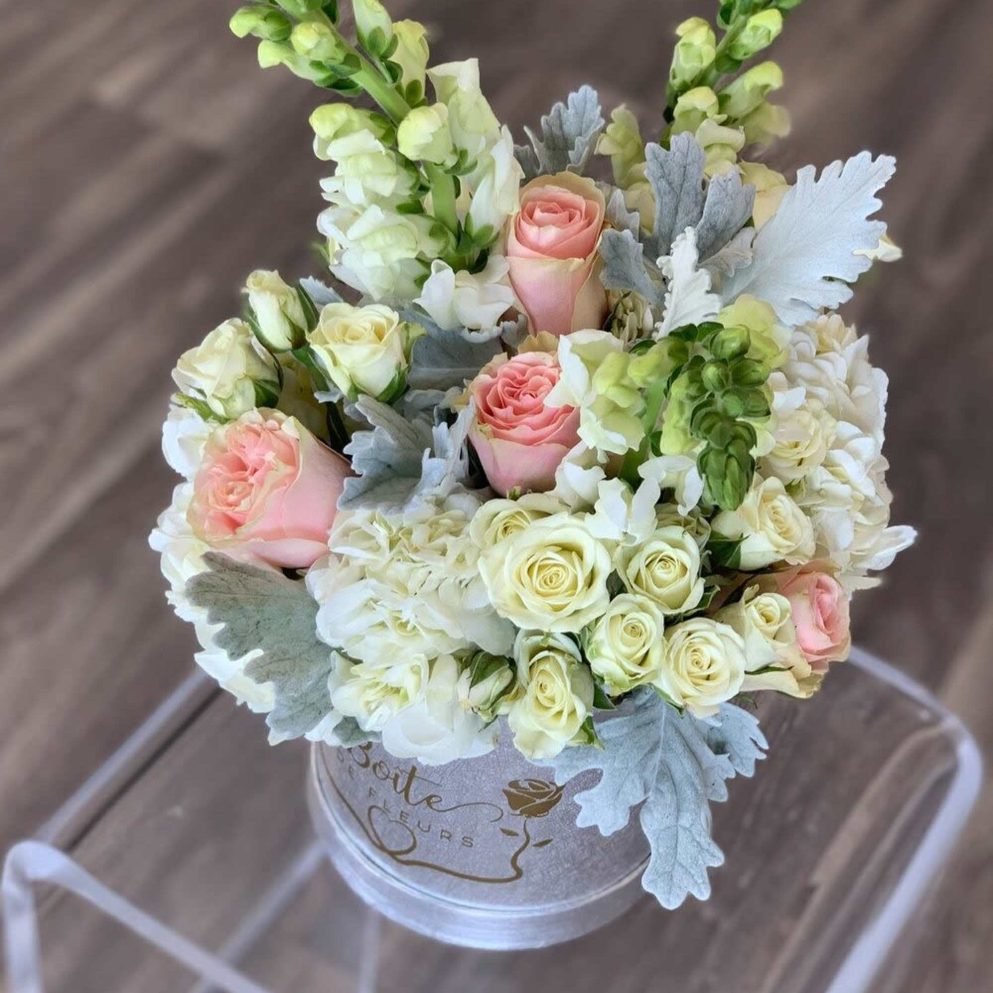 Pink and white roses in a round box with silver foliage