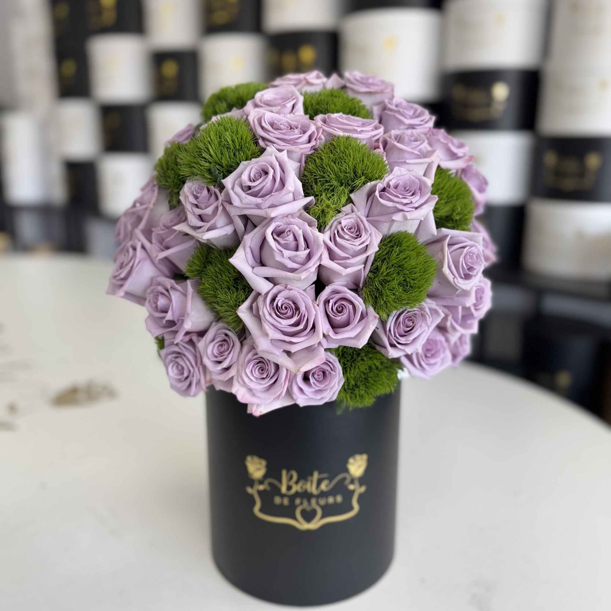 Lavender roses arranged with green pom-pom accents in a black hat box