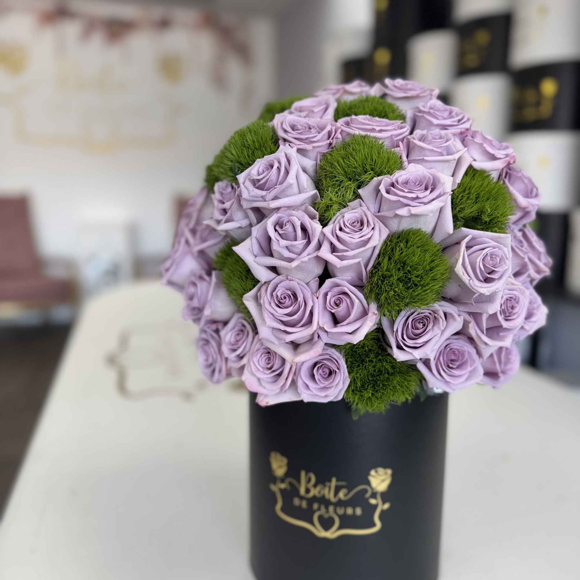 Lavender roses arranged with green moss in a black cylindrical box