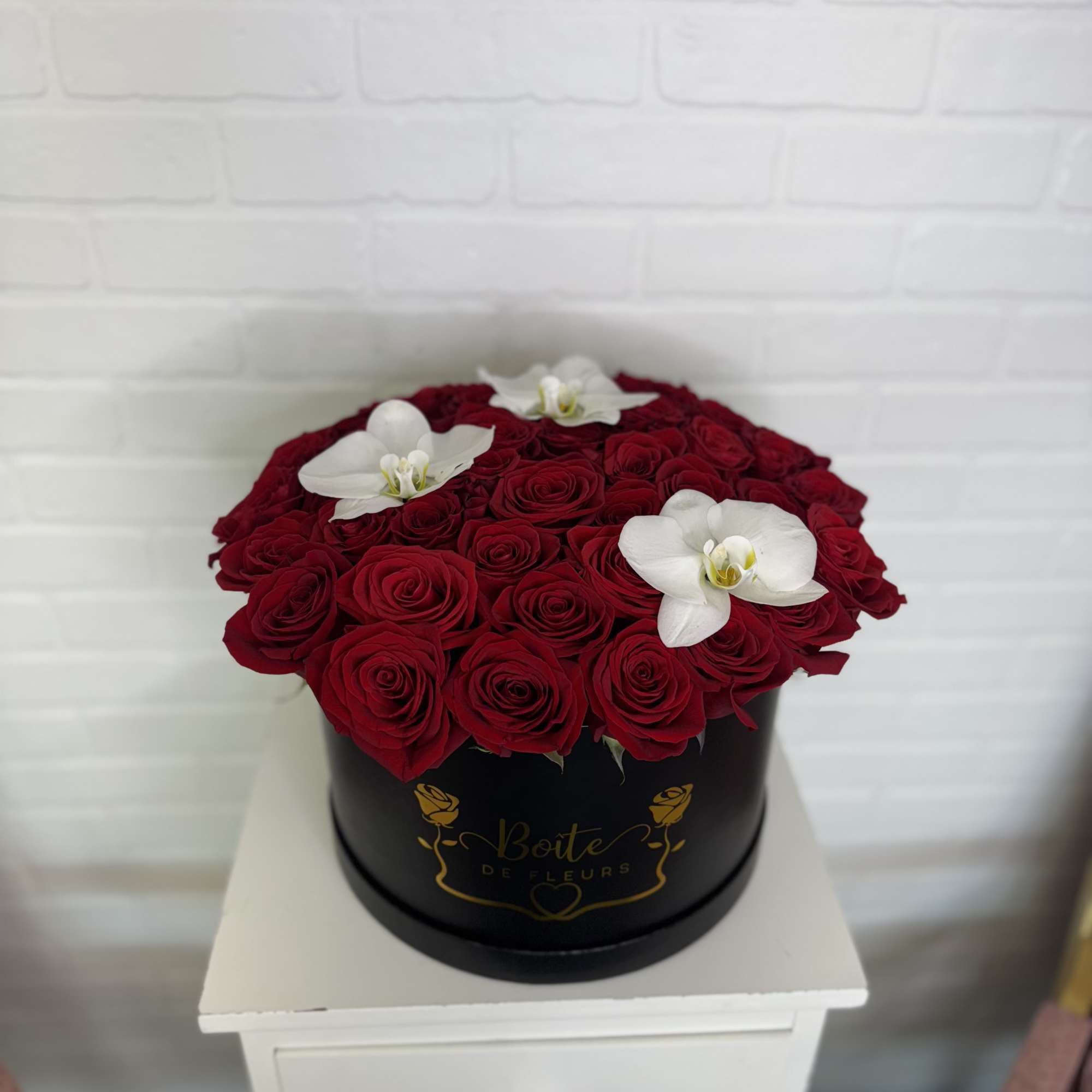 Round box of red roses topped with white orchids