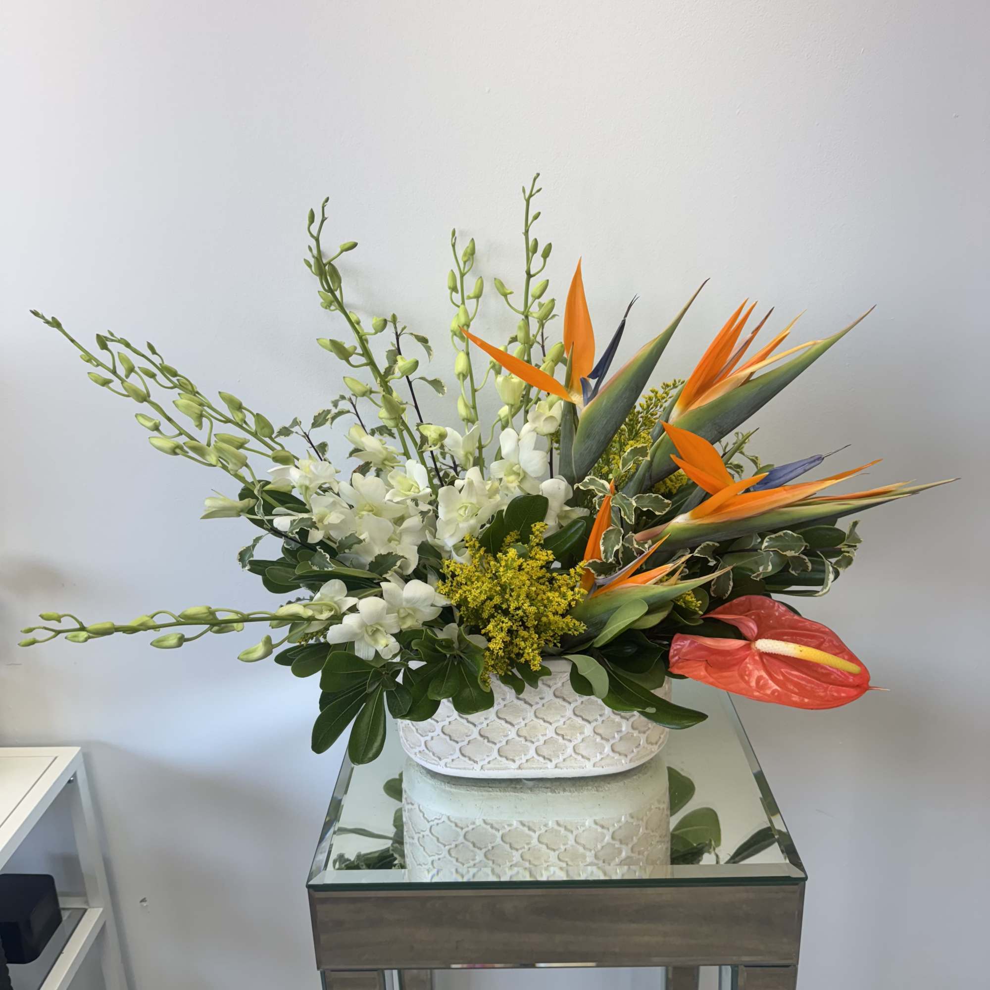 Tropical floral arrangement with white orchids and orange bird-of-paradise in a white vase