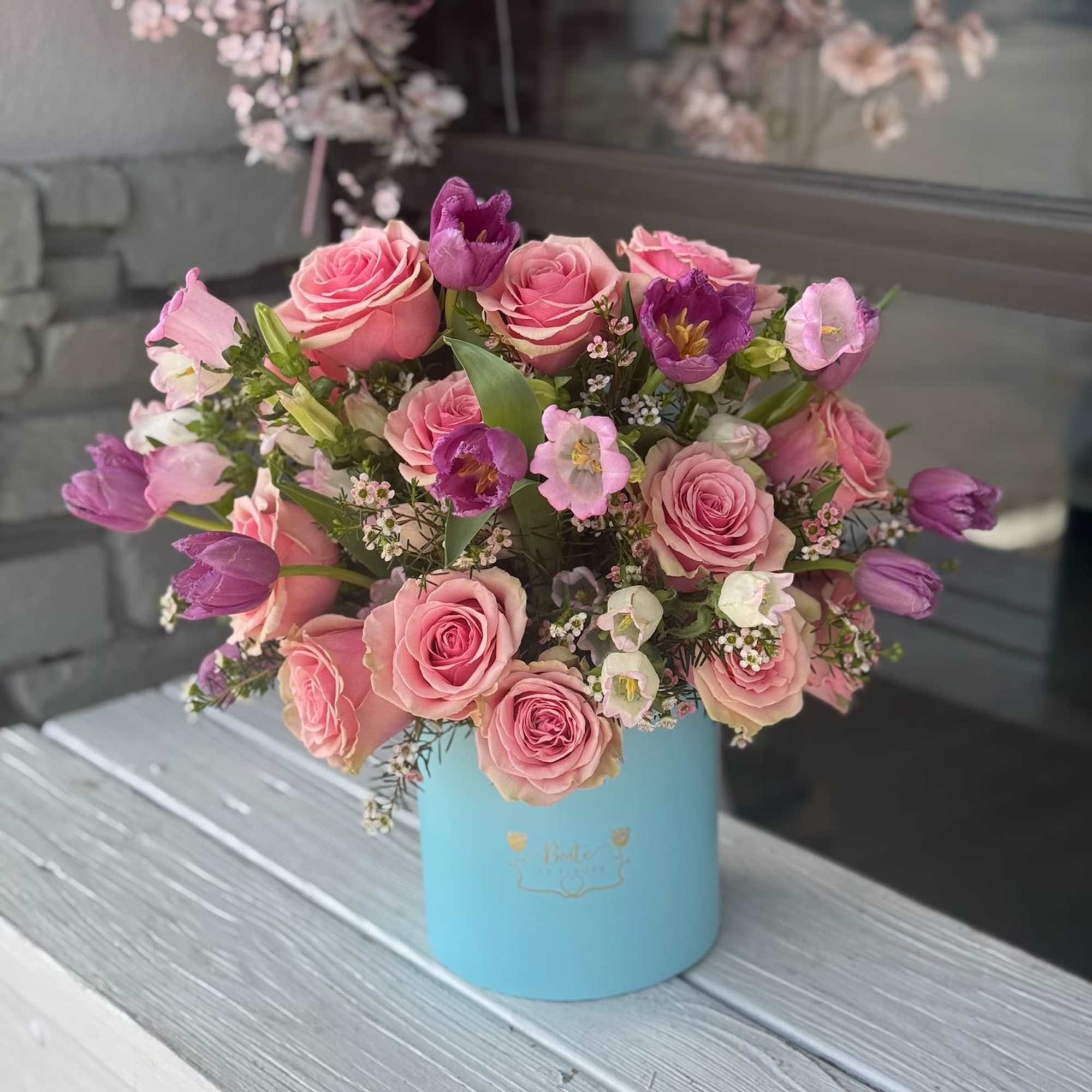 Pink roses and purple tulips arranged in a blue hat box