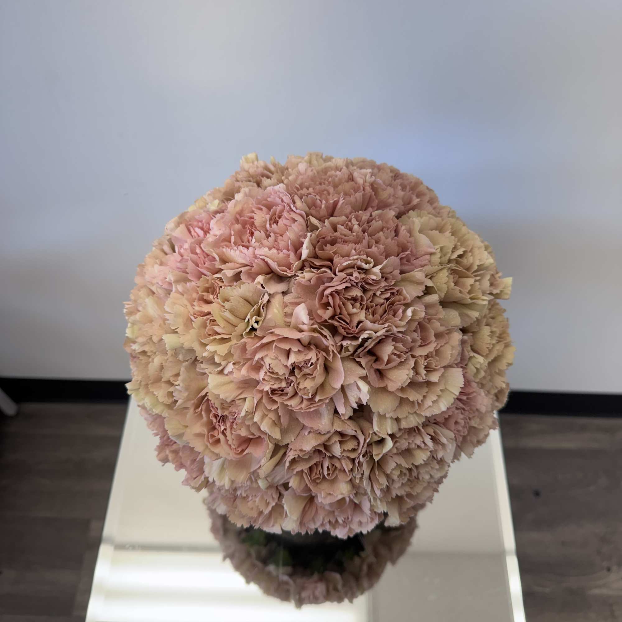 Round bouquet of pale pink and cream carnations on a mirrored stand