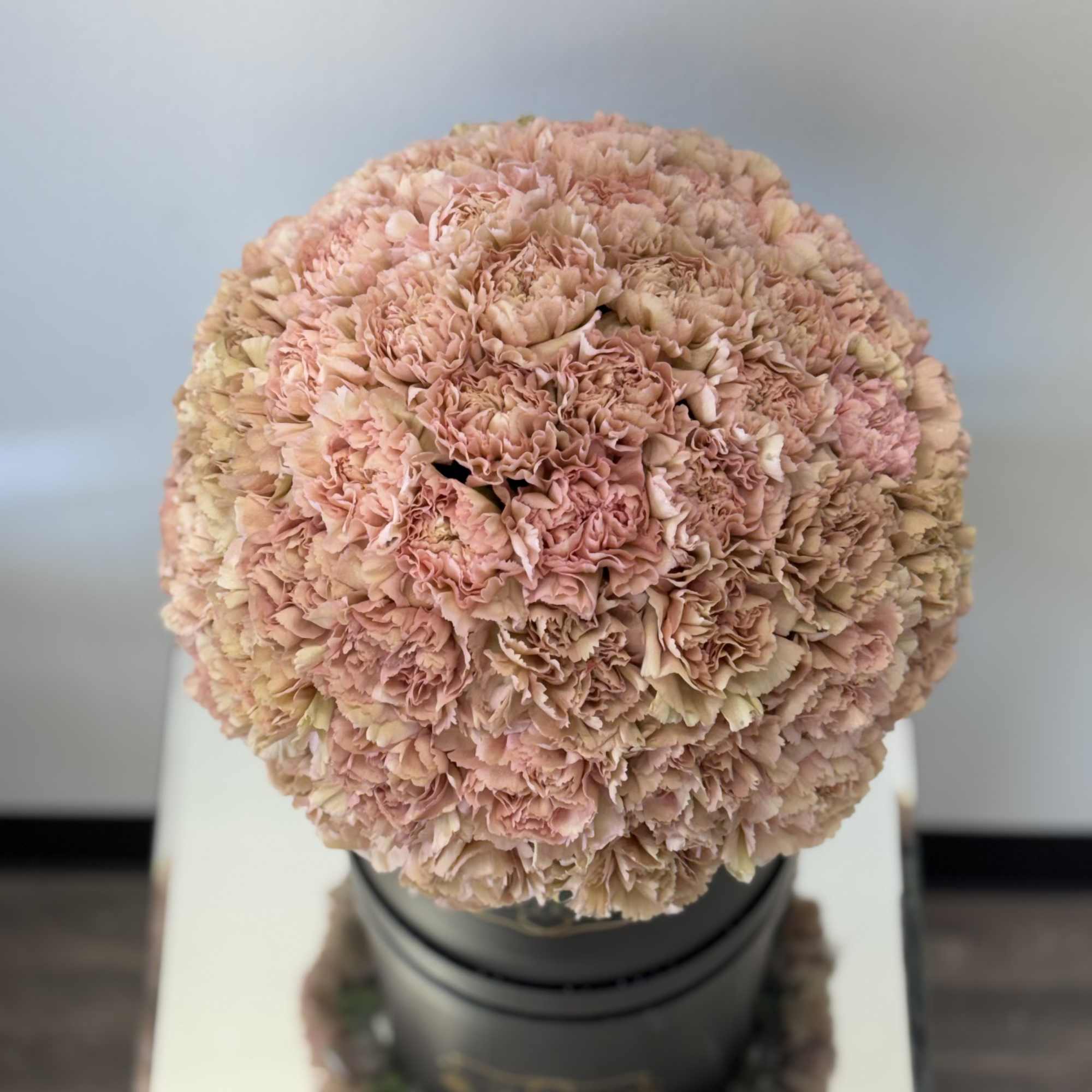 Round bouquet of pale pink carnations in a black container