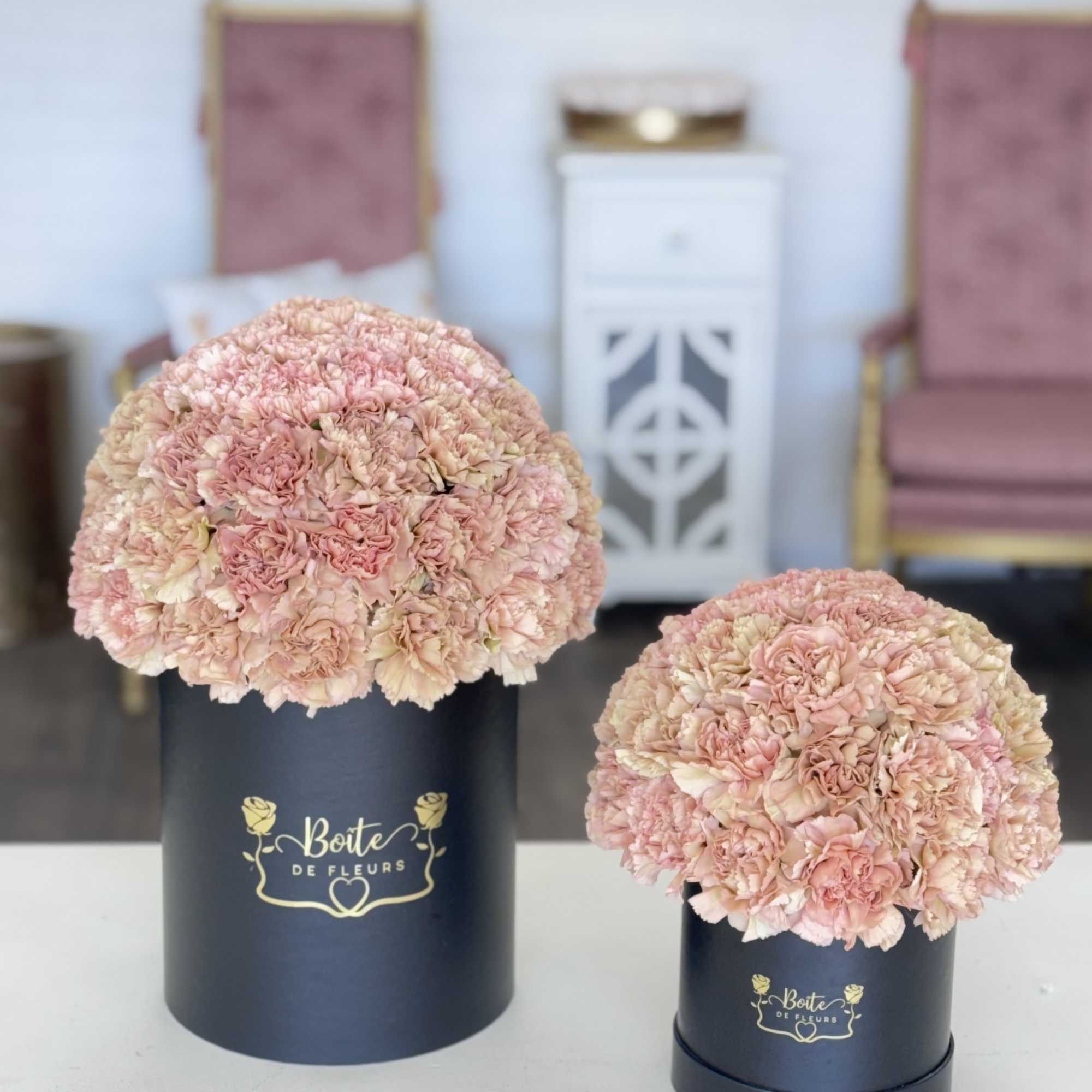 Two round pink carnation arrangements in black hat boxes