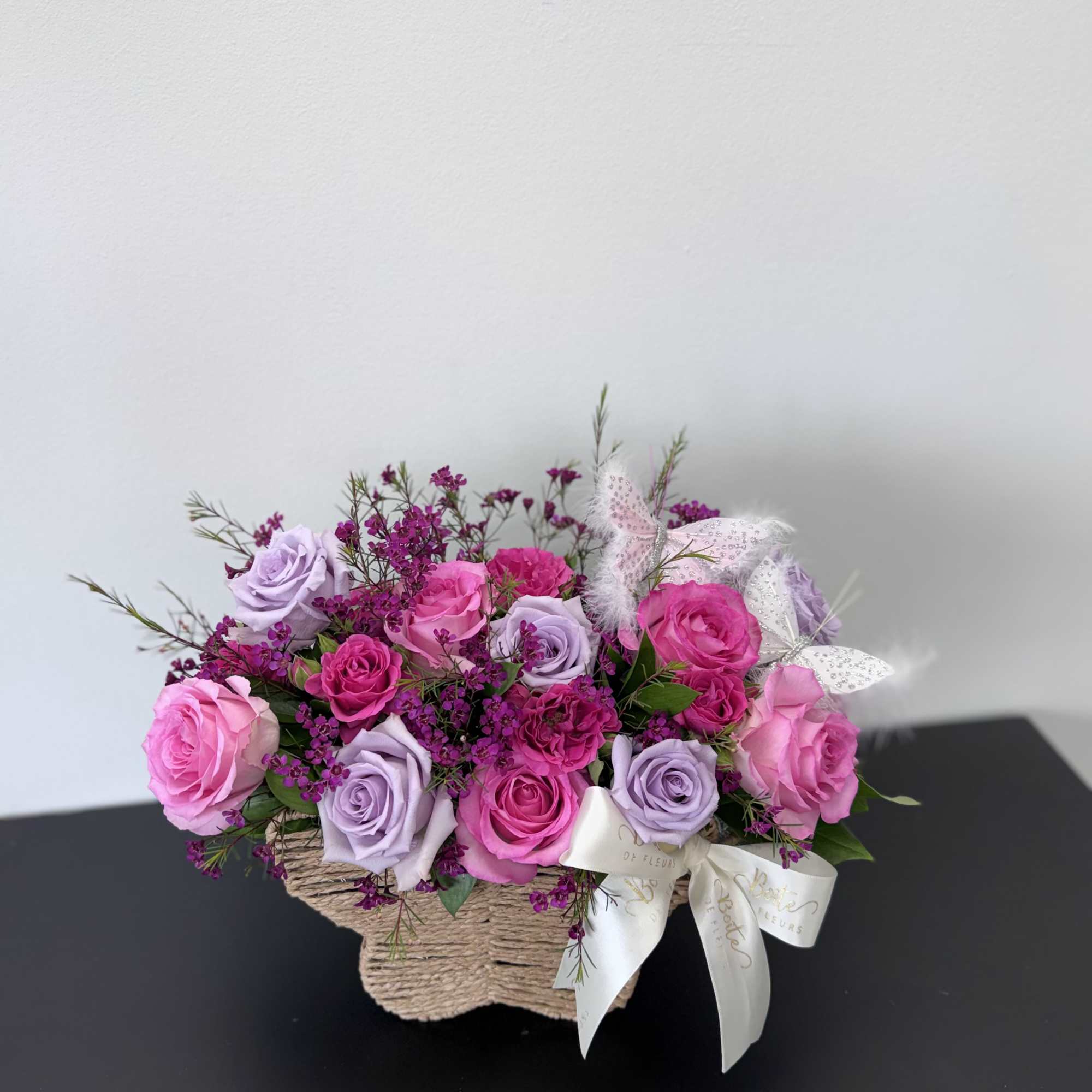 Pink and lavender roses arranged in a woven basket with a ribbon bow.