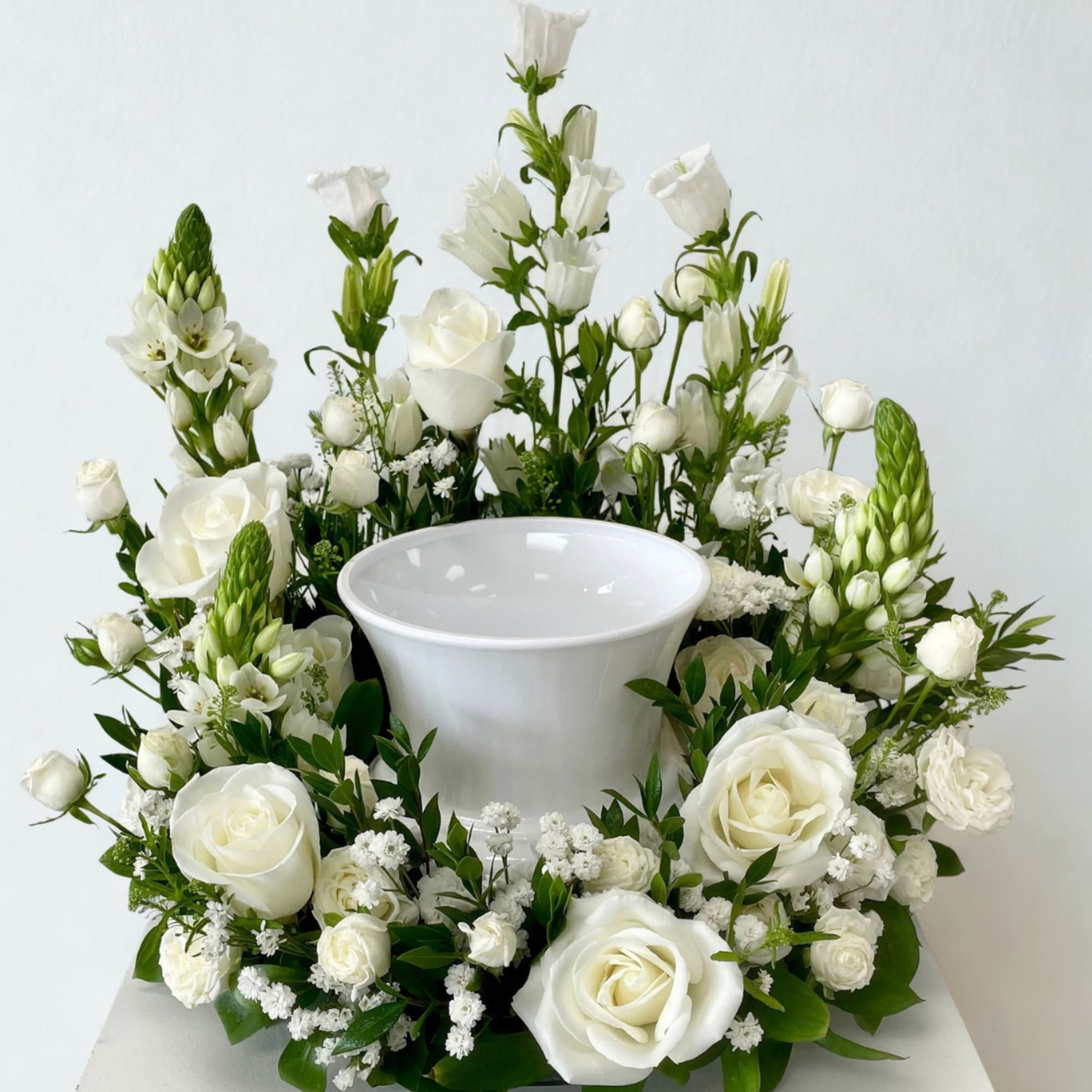 White roses and mixed white flowers arranged around a white urn vase