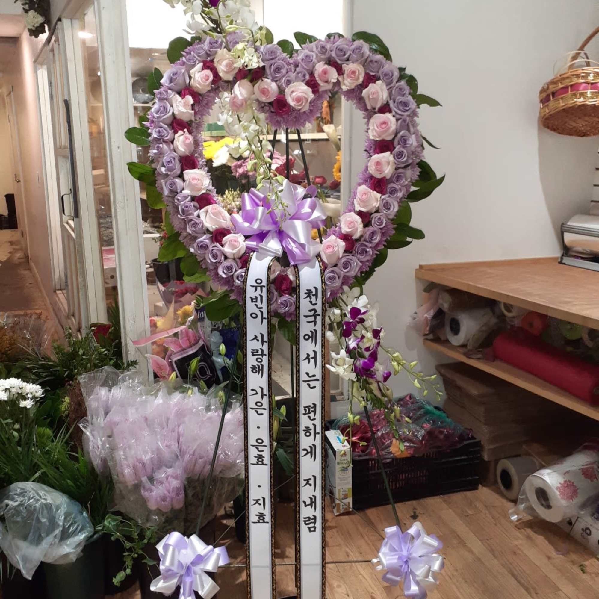 Heart-shaped floral wreath with purple and pink roses on a stand