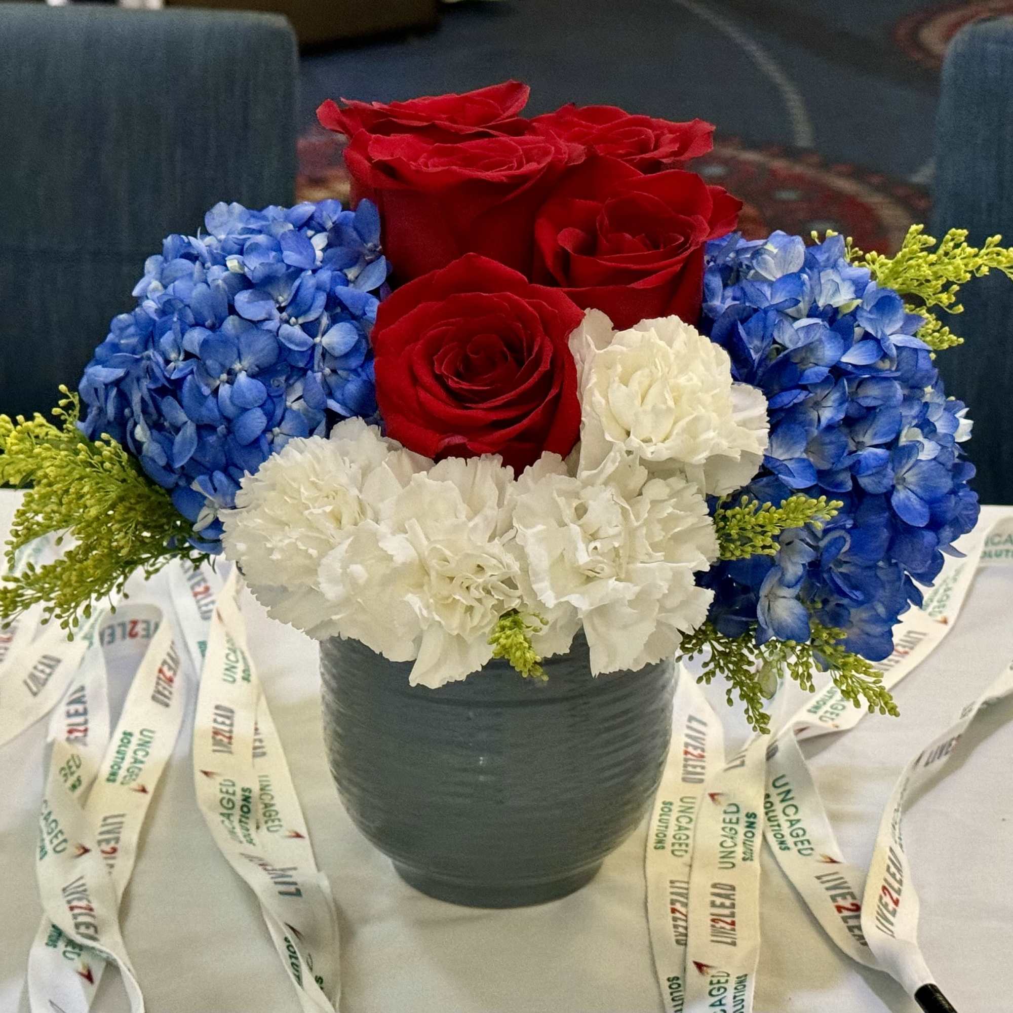 Red roses, blue hydrangeas, and white carnations in a dark vase