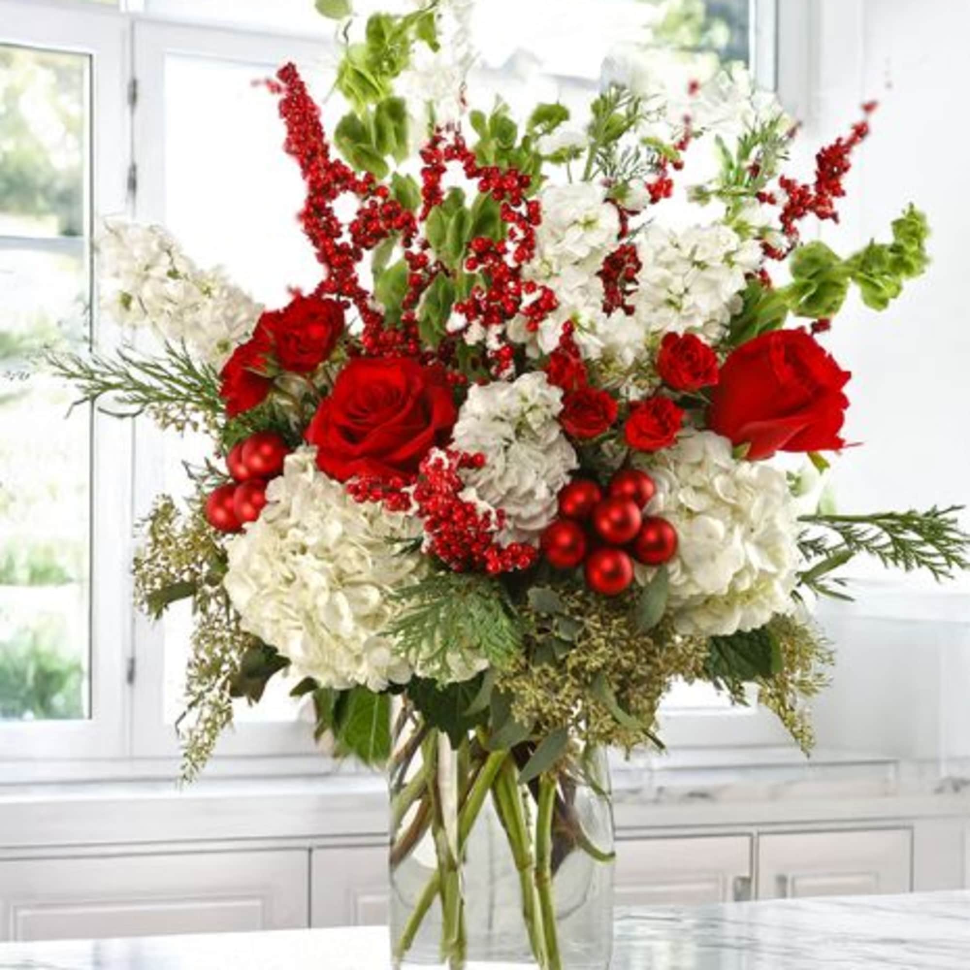 Red roses and white hydrangeas in a clear glass vase with red berry accents