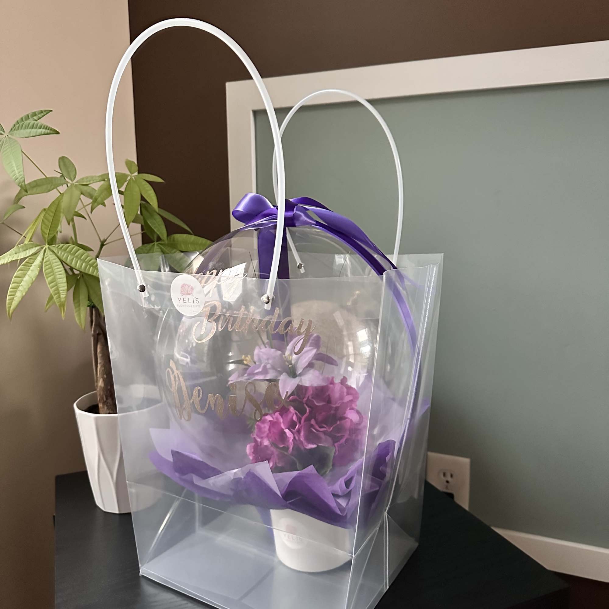 Purple floral gift in a clear handled bag with a birthday balloon