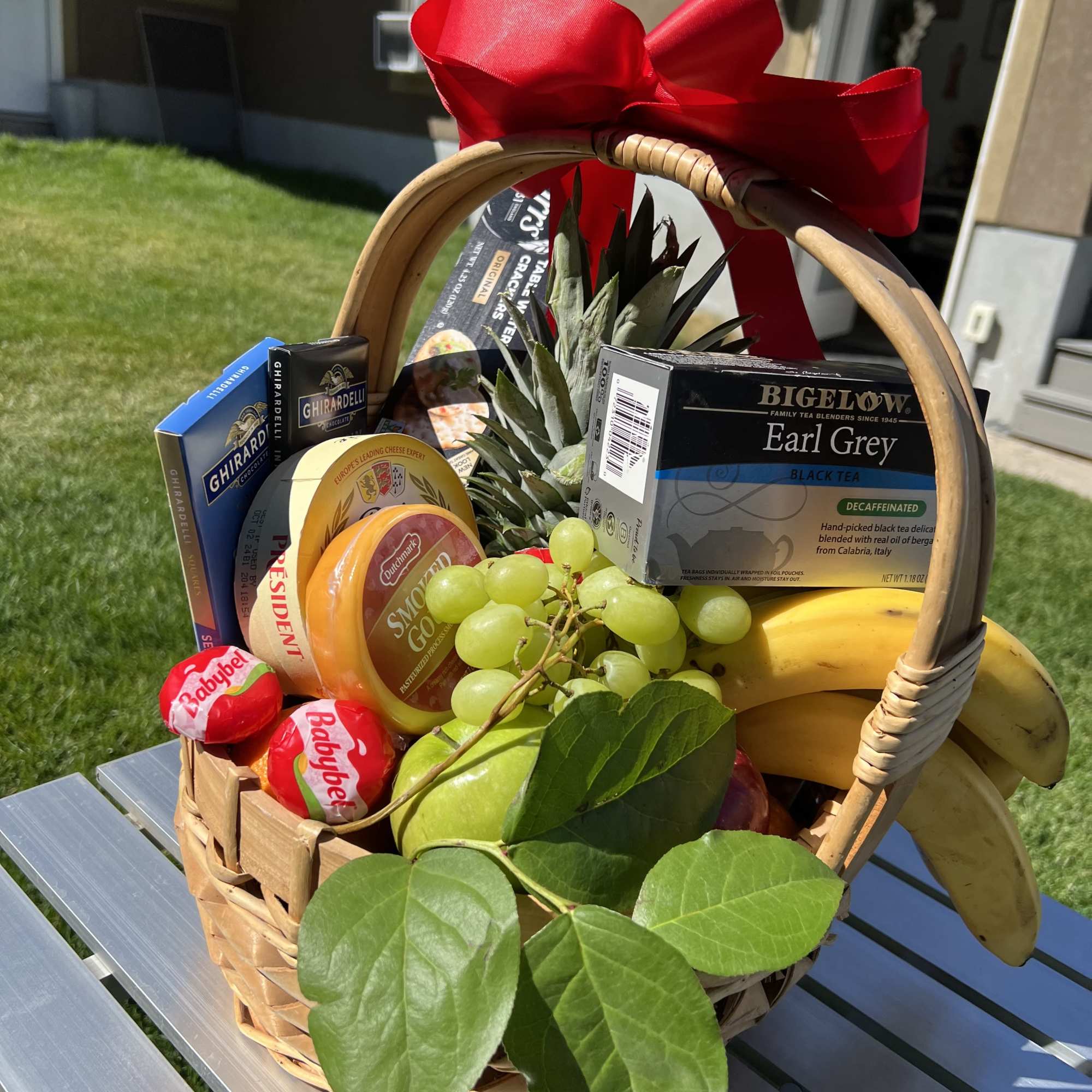 Gift basket with fruit, tea, cheese, and chocolates tied with a red bow