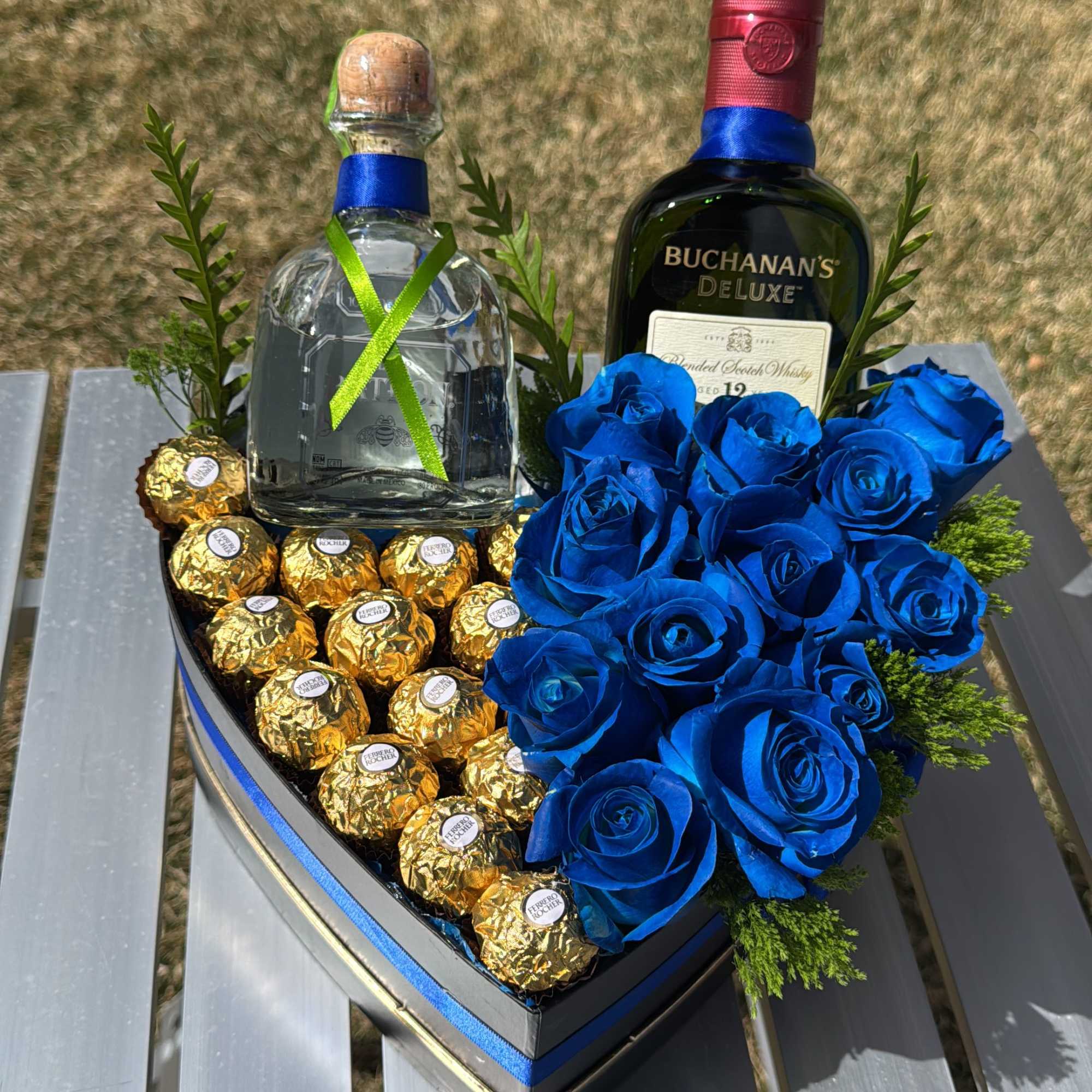 Heart-shaped gift box with blue roses, chocolates, and two liquor bottles