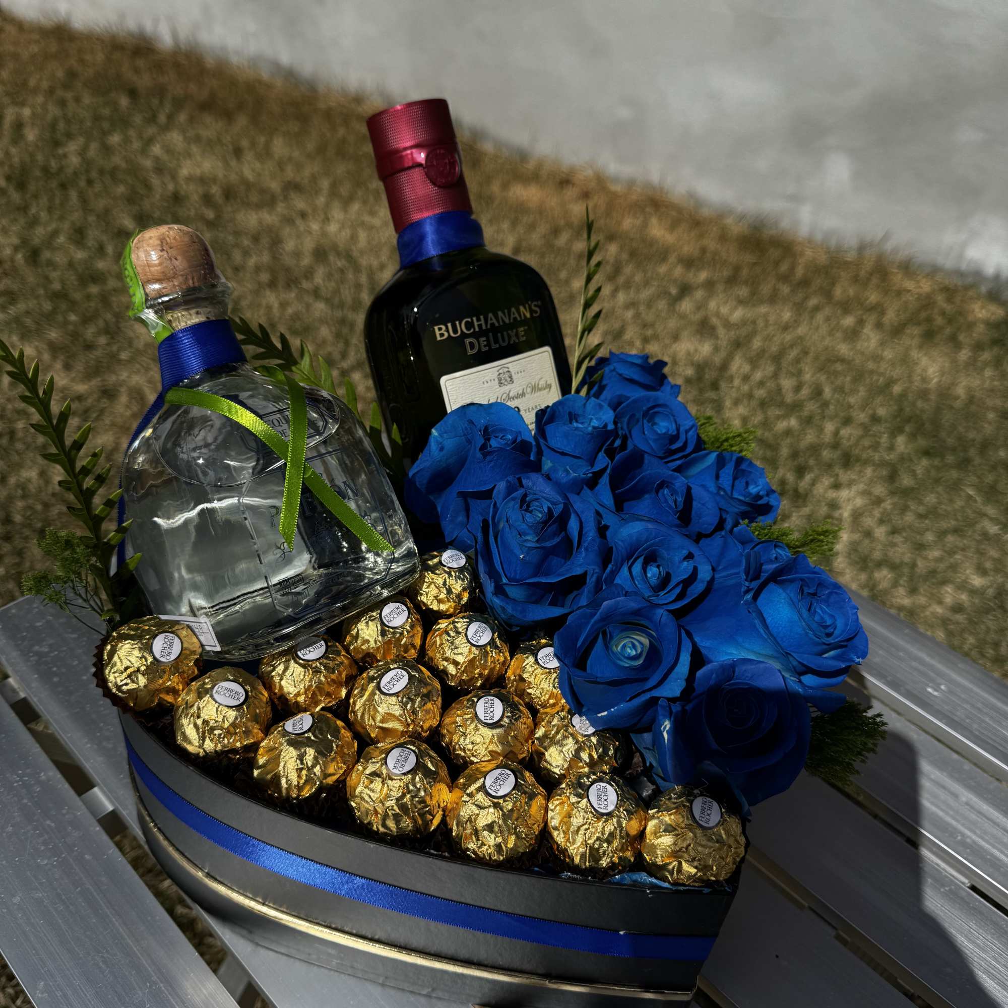 Heart-shaped gift tray with blue roses, chocolates, and two liquor bottles
