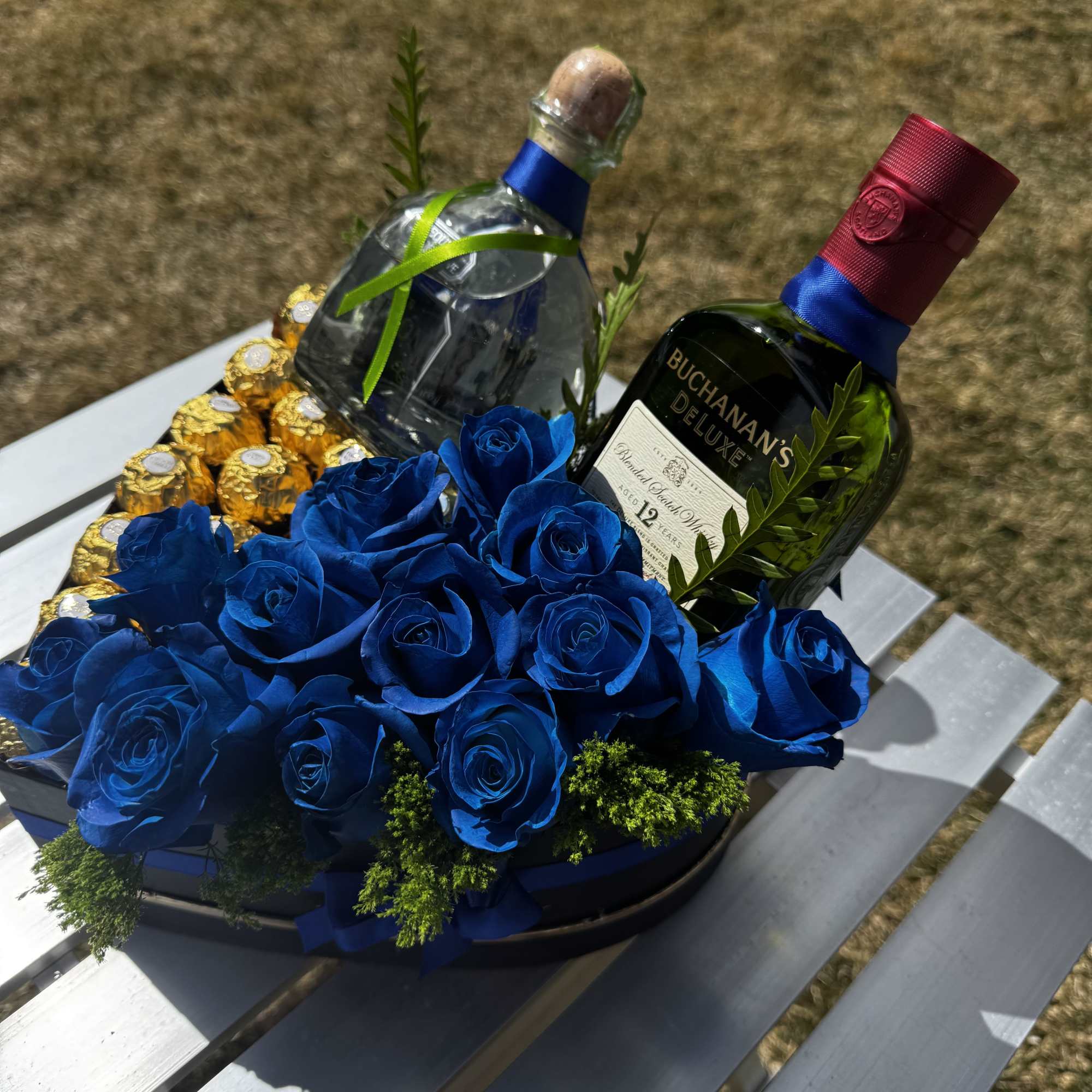 Blue roses arranged with two liquor bottles and chocolates on a tray.