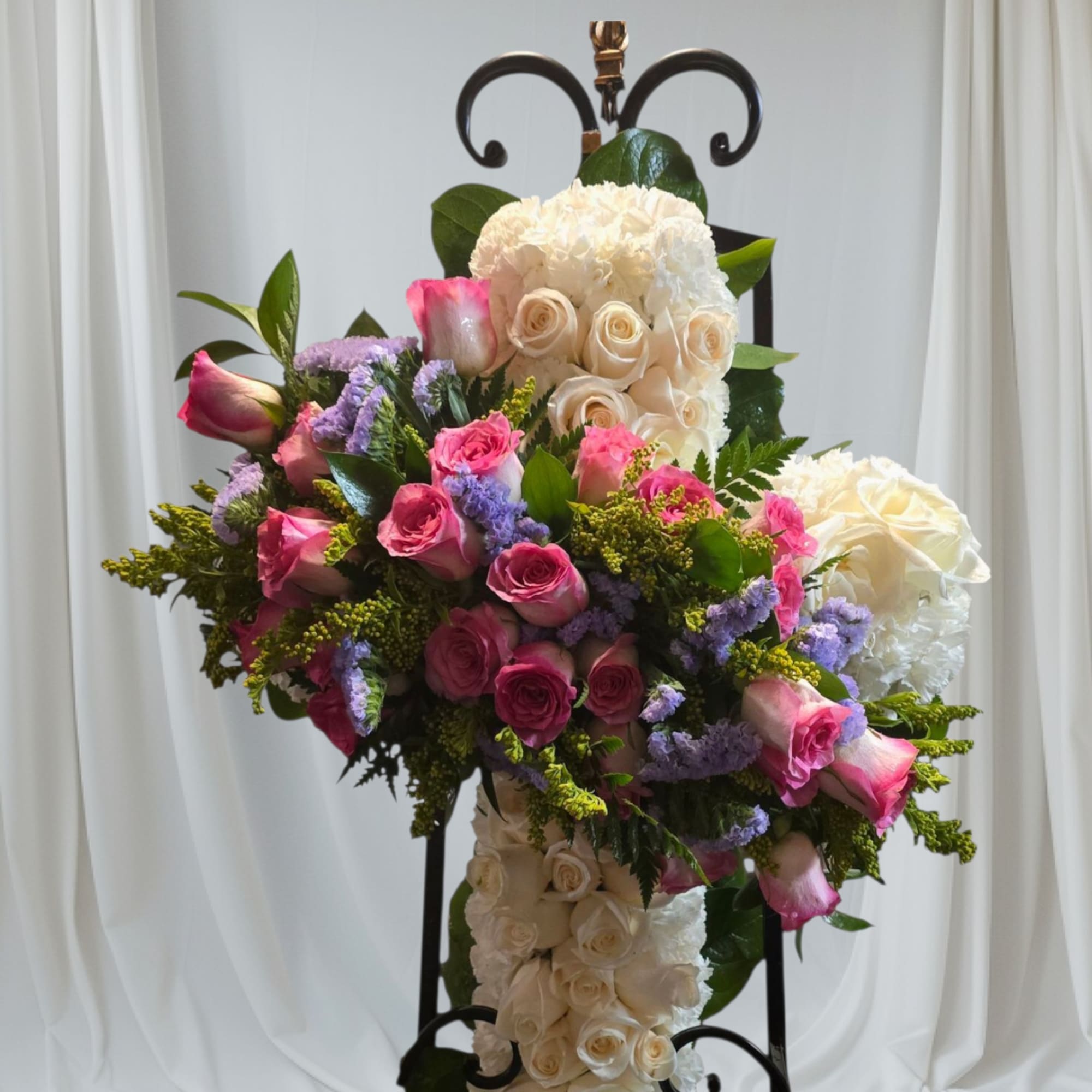 Floral cross arrangement with pink and white roses on a black stand