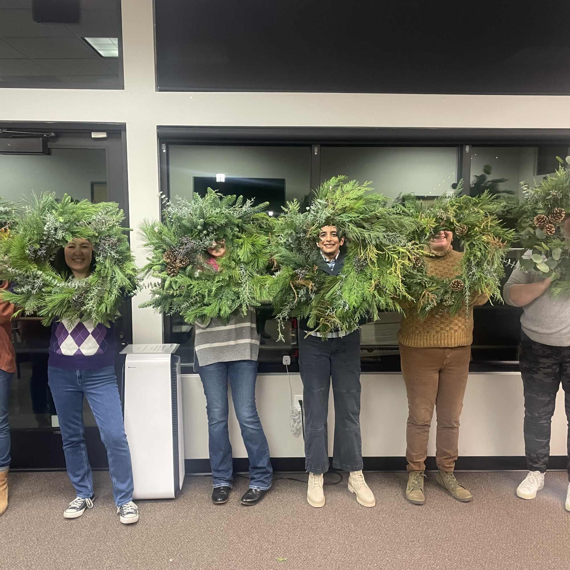 People holding large evergreen wreaths indoors