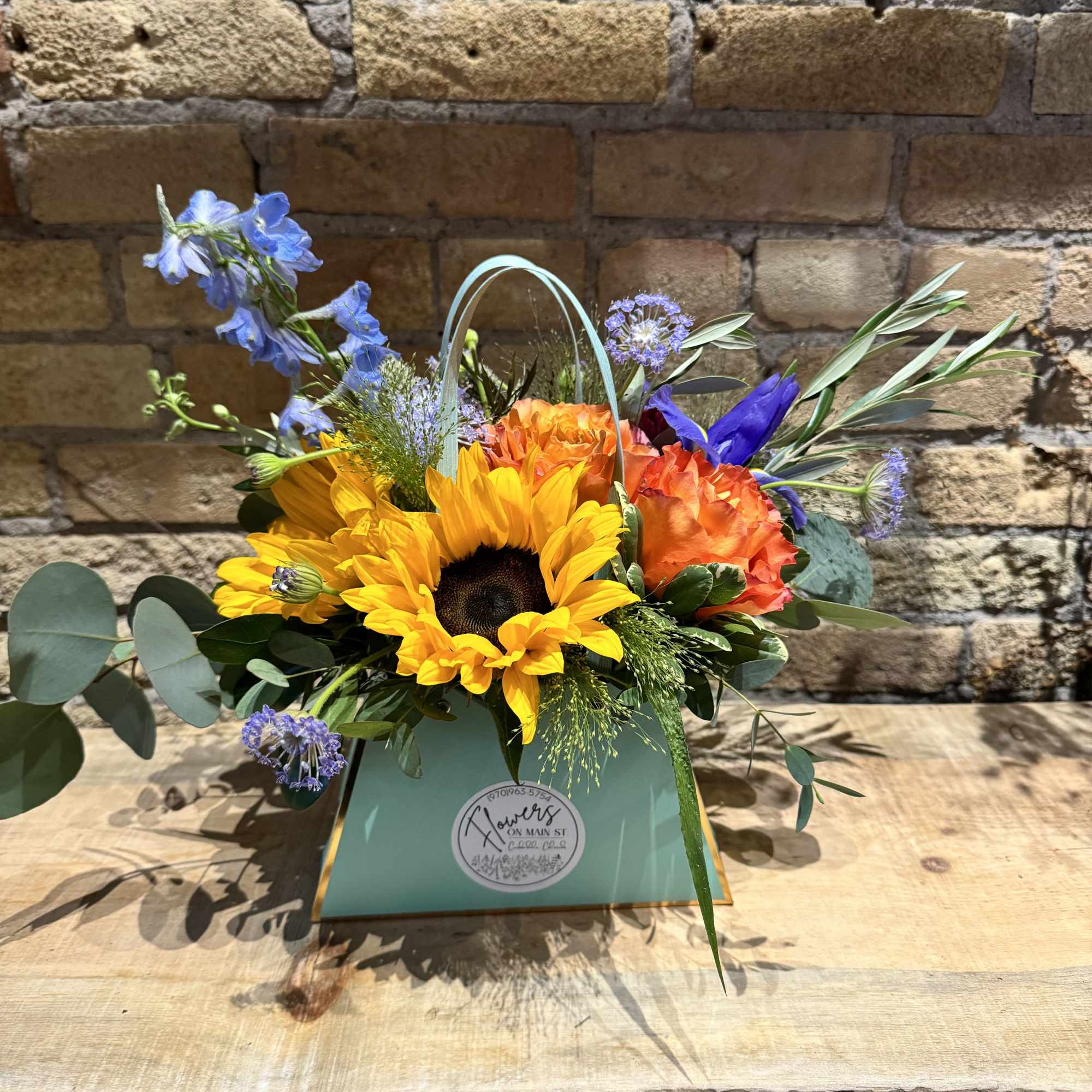 Bright mixed bouquet in a mint gift bag with sunflowers and orange blooms