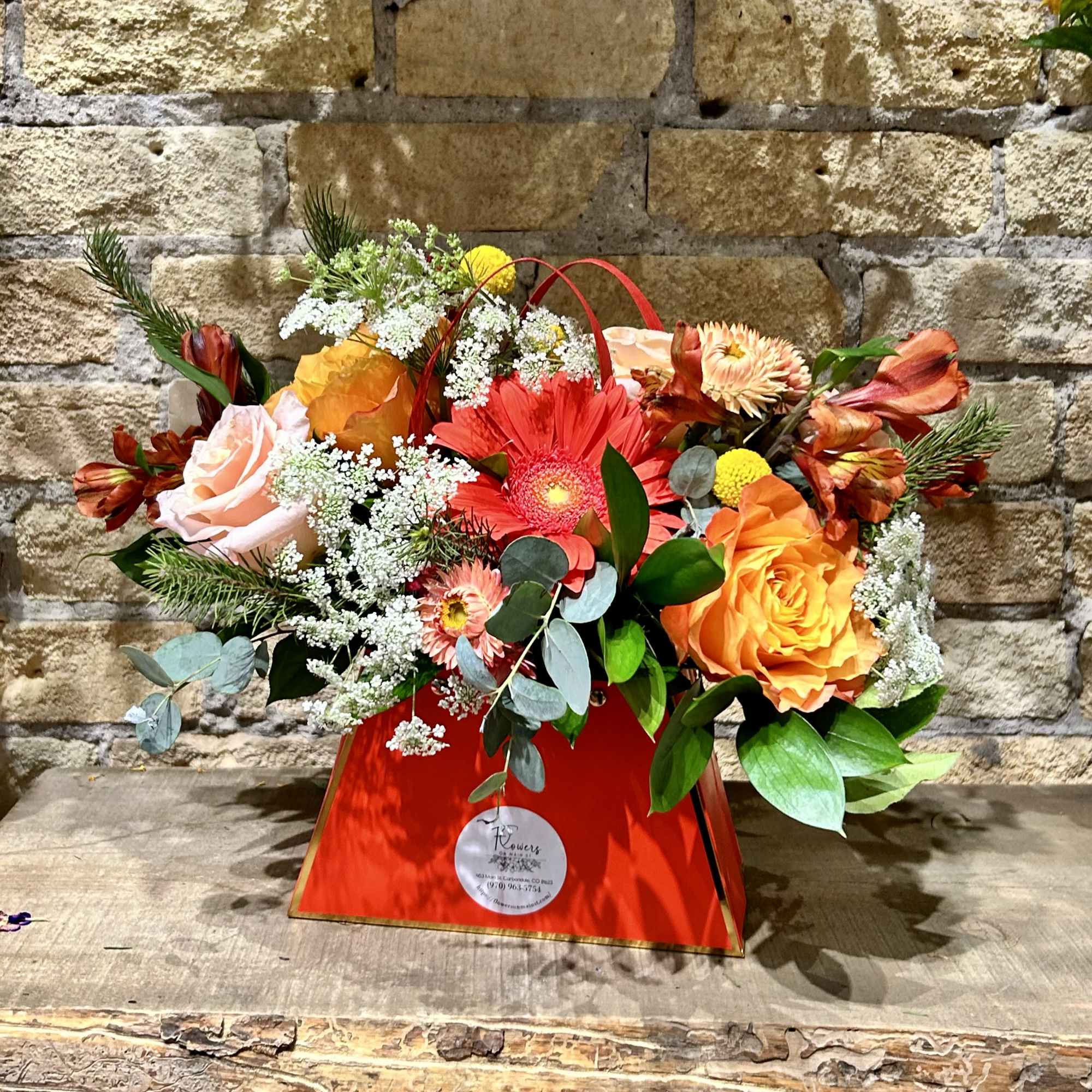 Mixed bouquet in a red handled gift bag with orange and pink flowers