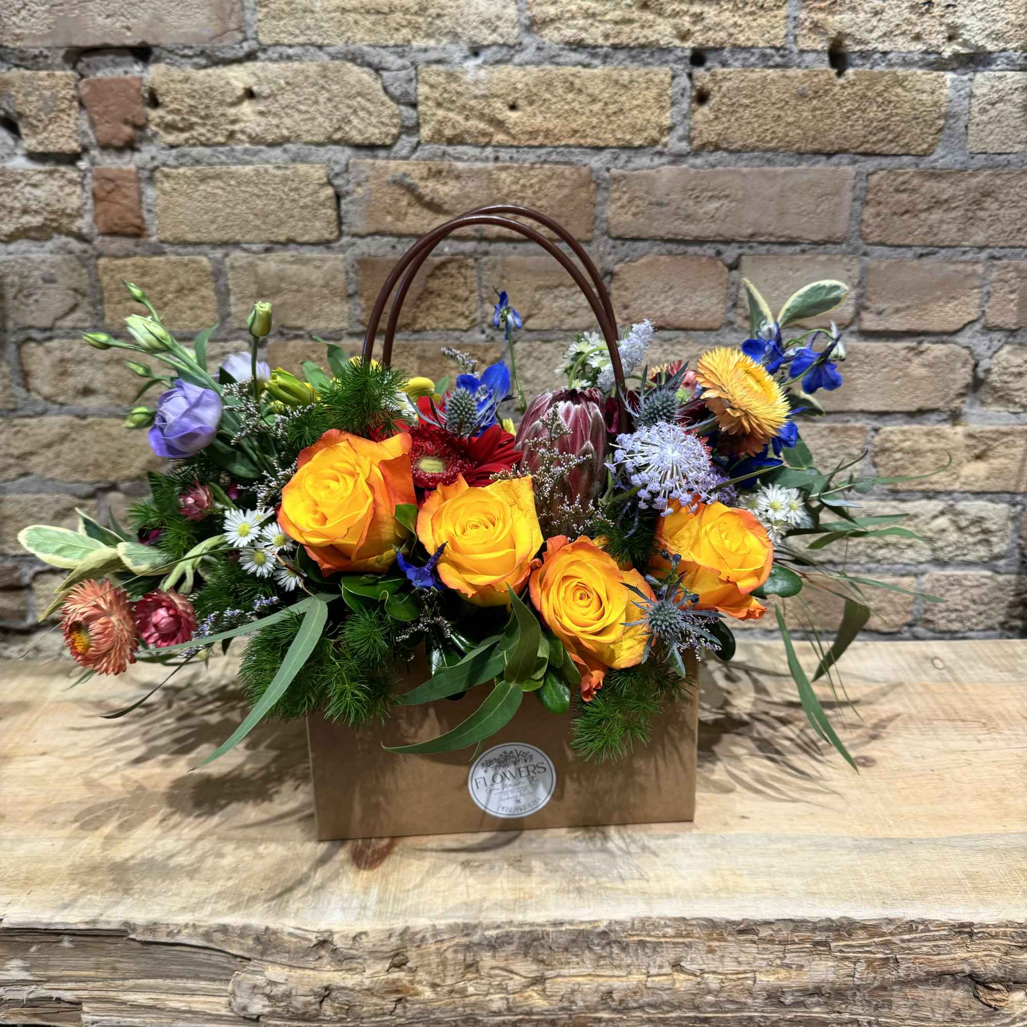 Mixed flower arrangement in a brown handled gift bag