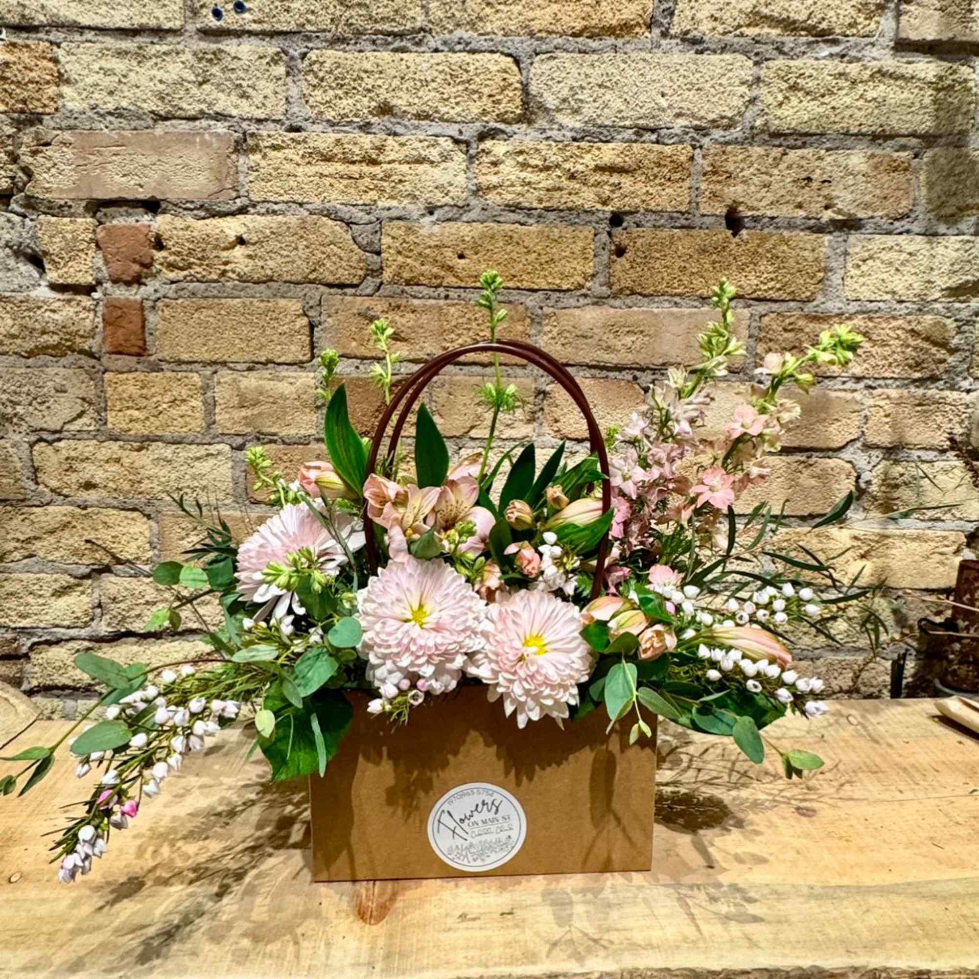 Pink and white flower arrangement in a brown handled box