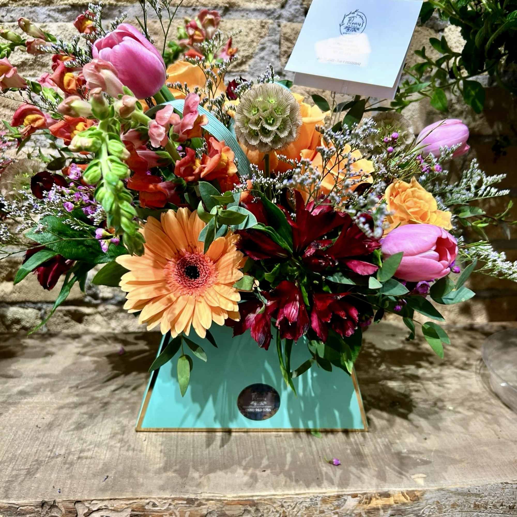 Colorful mixed flower arrangement in a turquoise box with a card