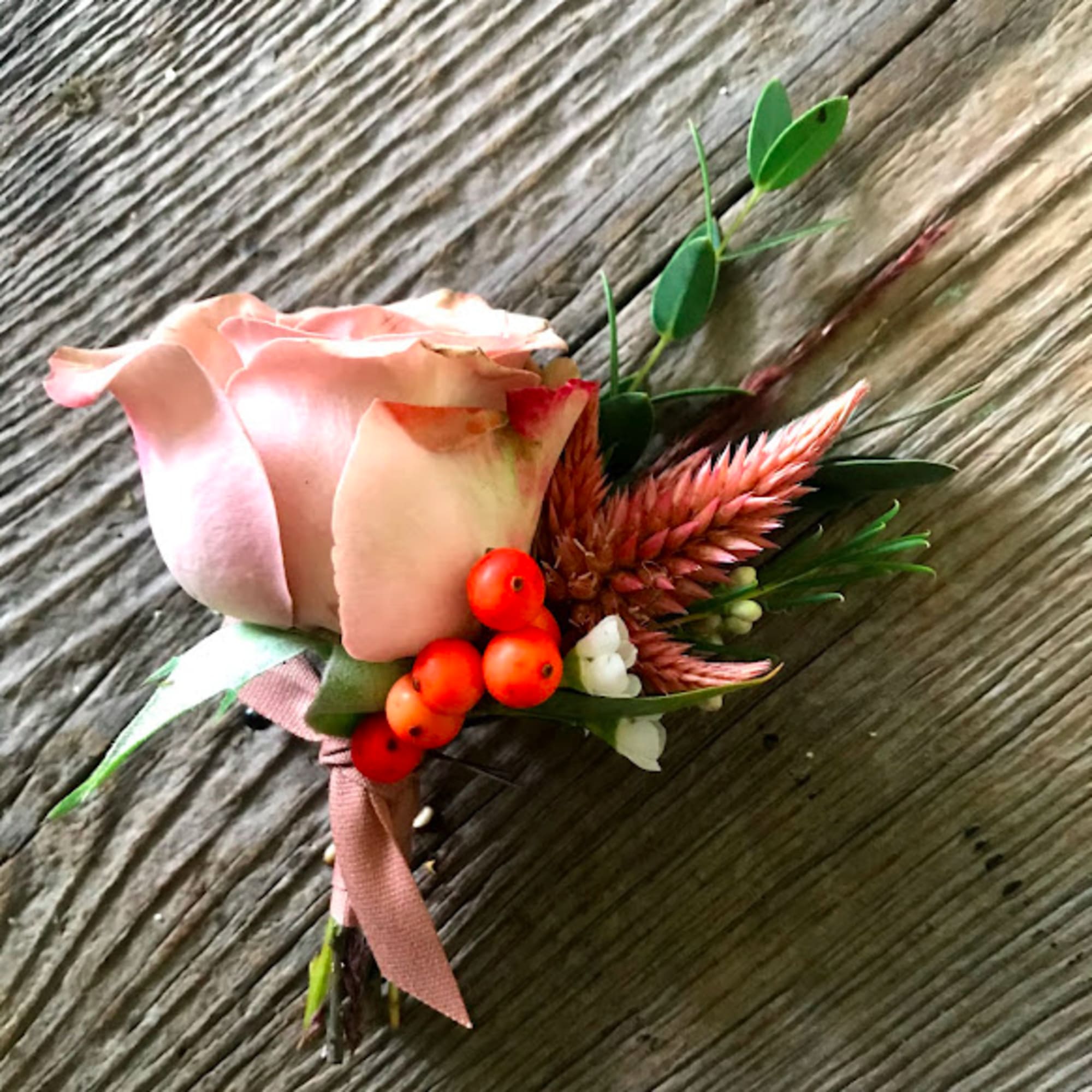 Pink rose boutonniere with orange berries and greenery