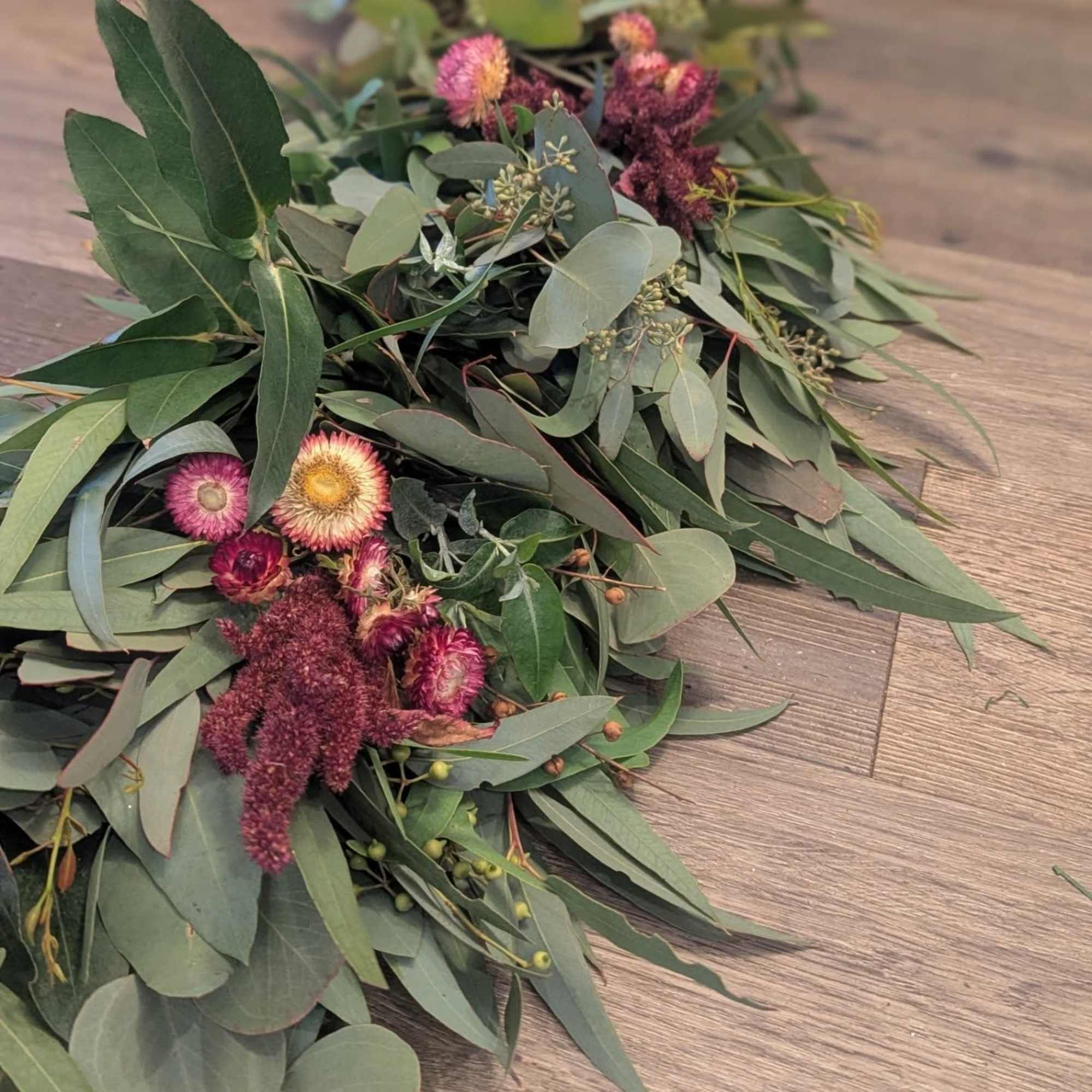 Long eucalyptus garland with clusters of small pink and yellow flowers on a wood surface