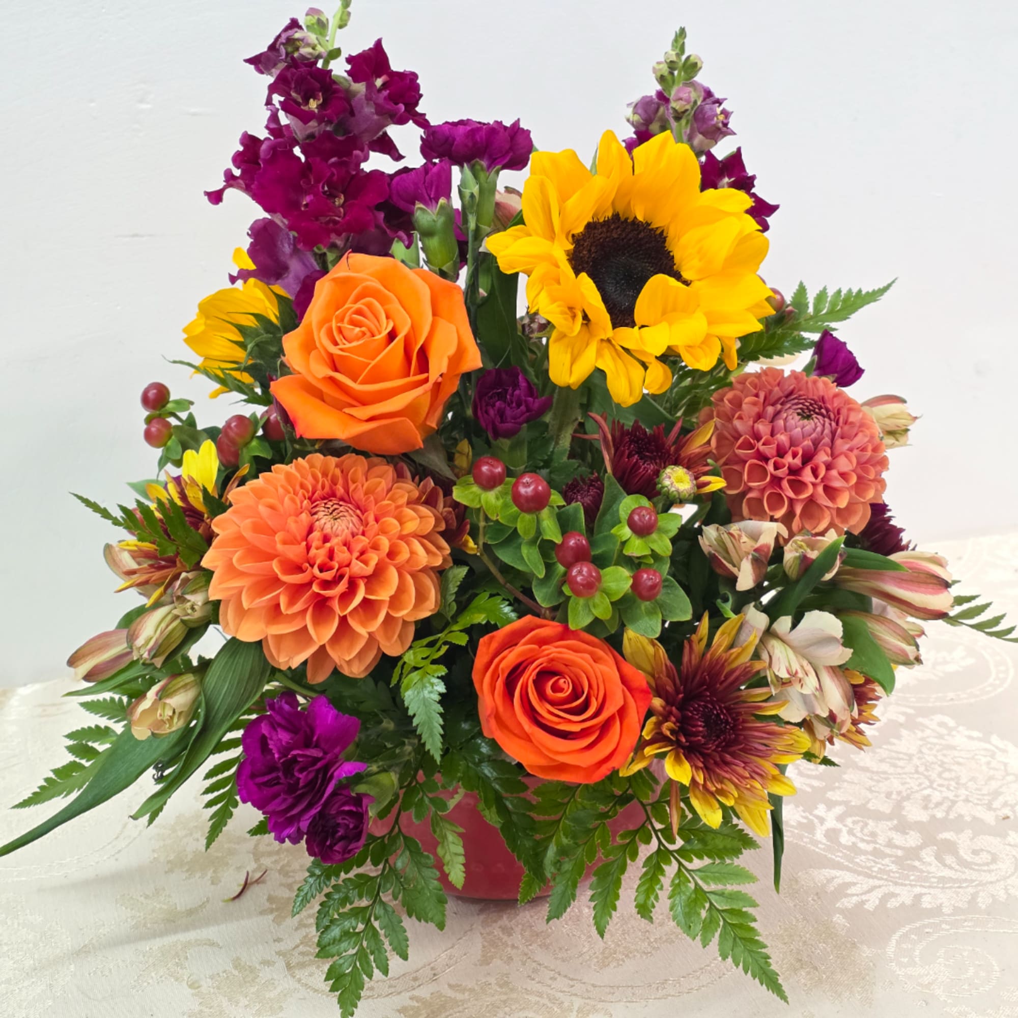 Mixed bouquet with orange roses, sunflowers, and purple blooms in a vase