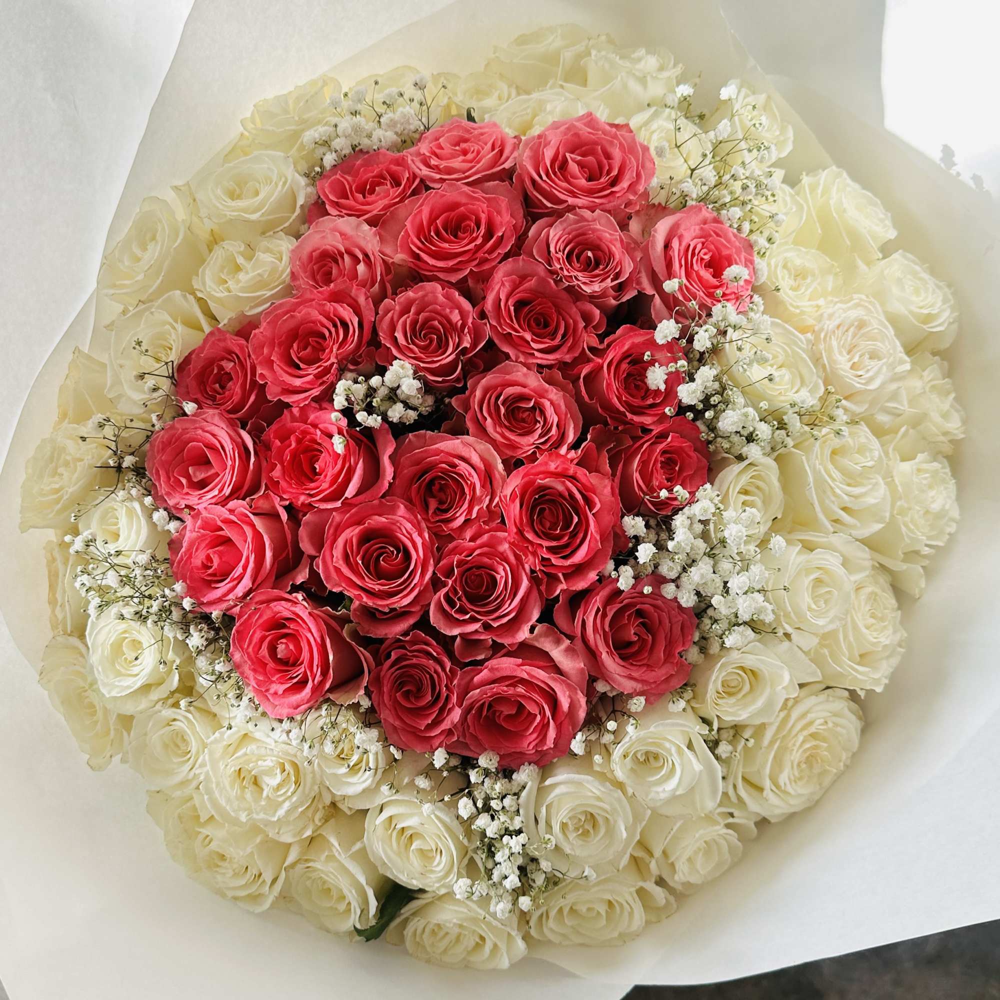 Round bouquet of pink roses in the center, ringed by white roses and baby's breath, wrapped in white paper