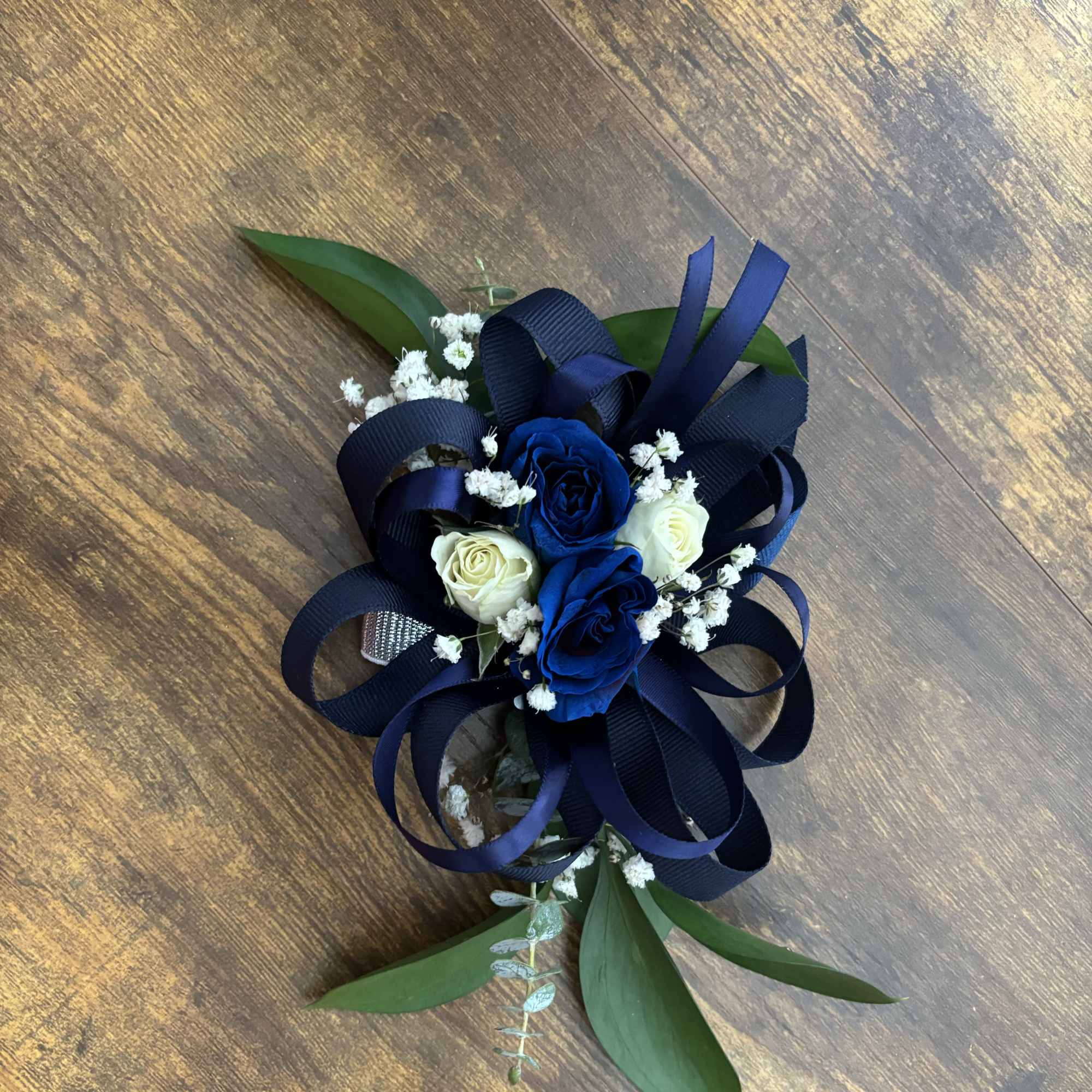 Blue and white rose corsage with navy ribbon and greenery