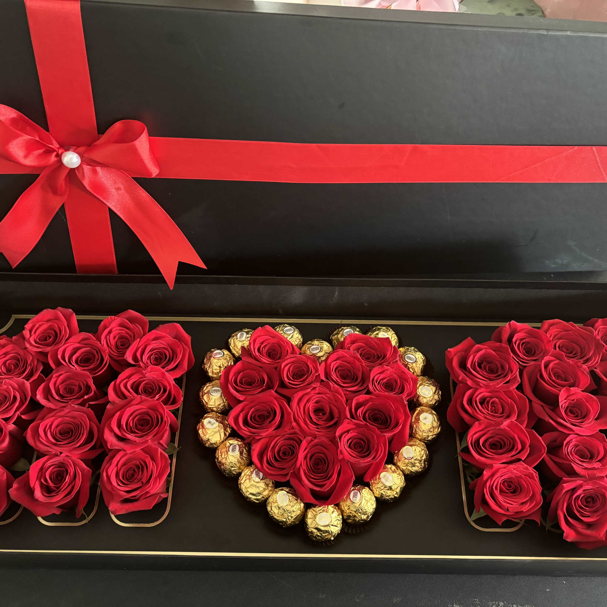 Black gift box with red roses and gold chocolates arranged in a heart