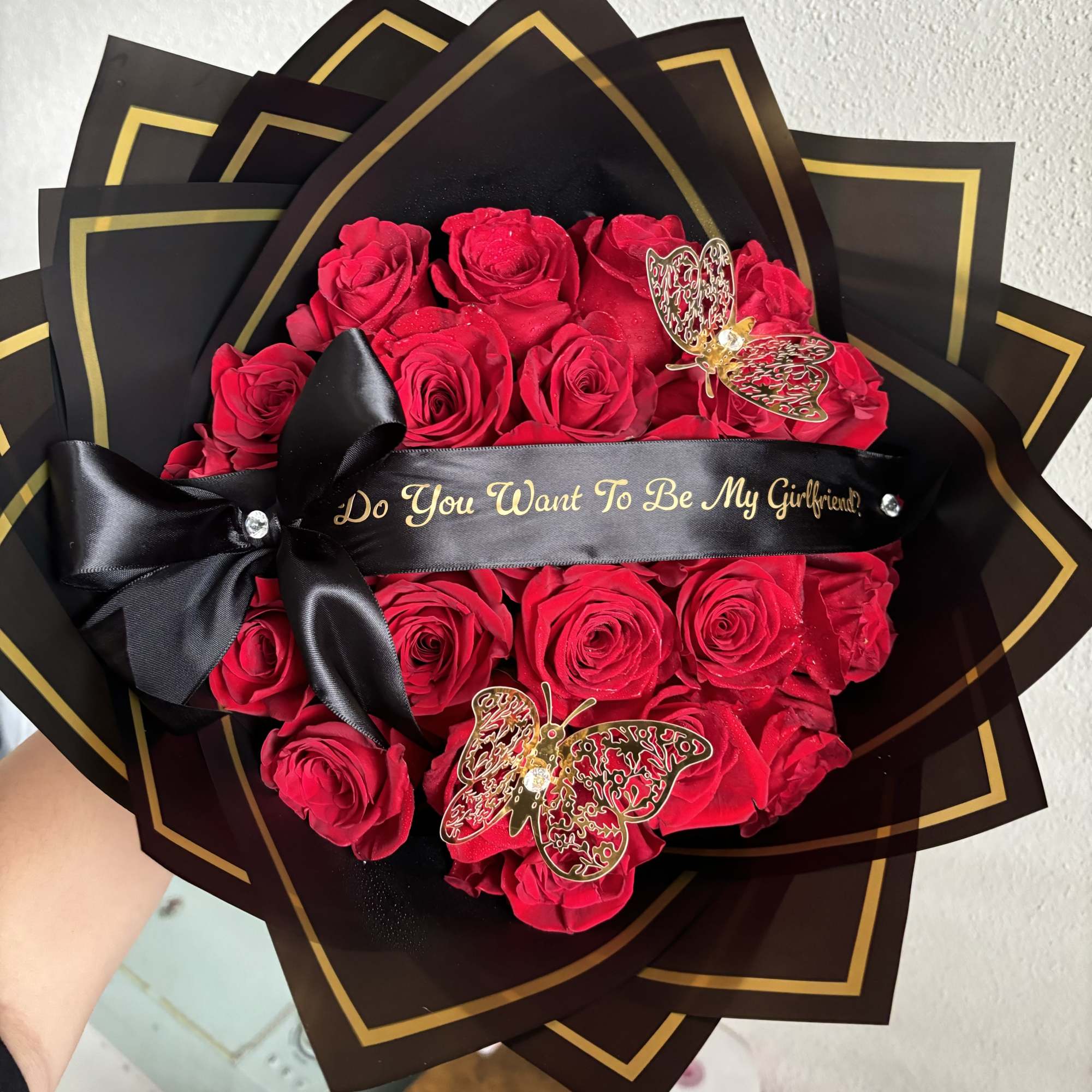Red roses wrapped in black paper with gold trim and a black ribbon