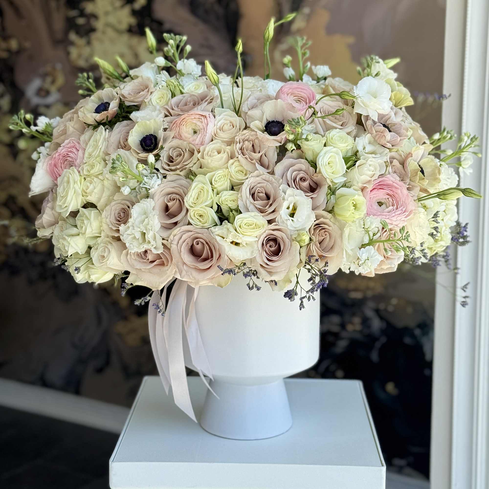 Blush and white rose arrangement in a white pedestal vase