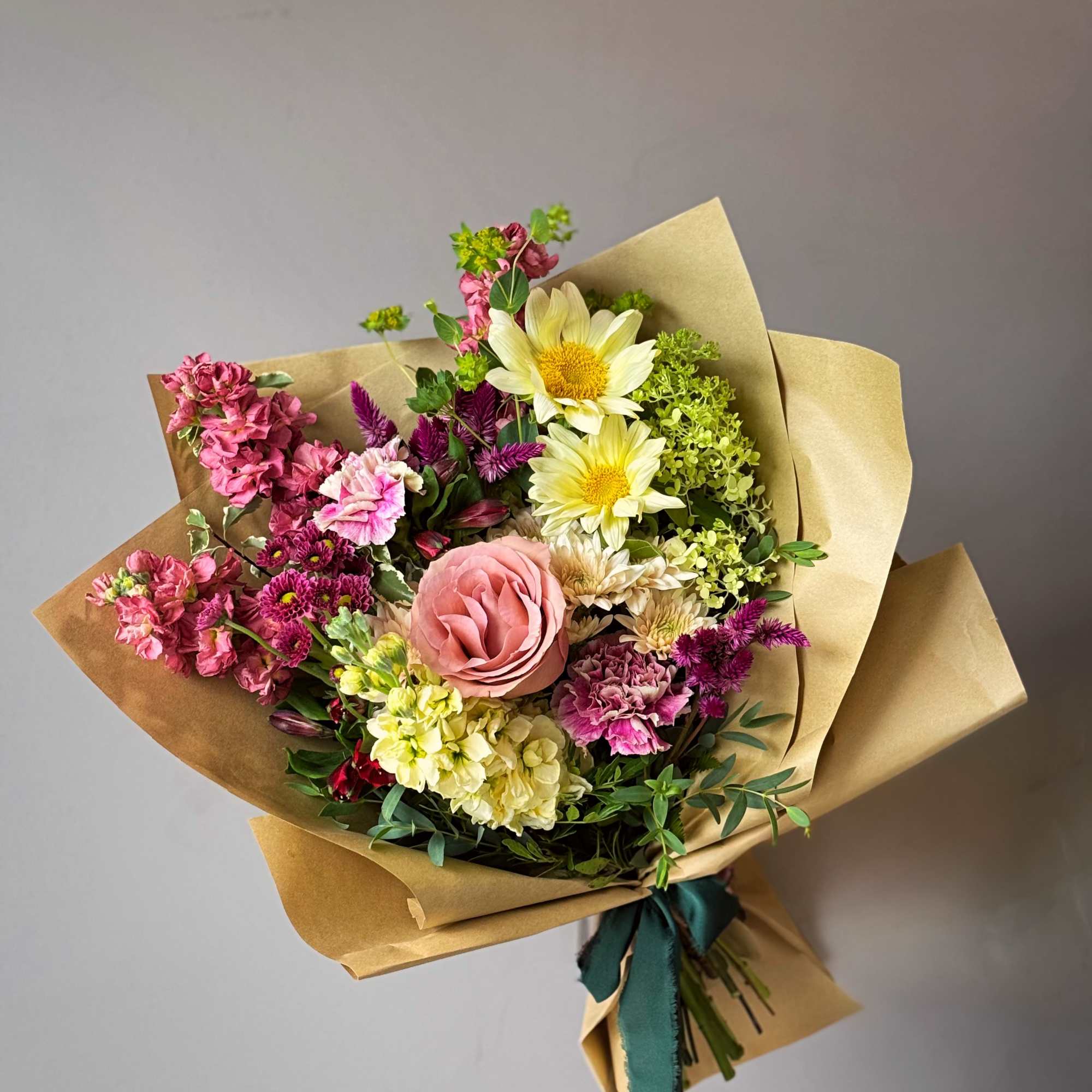 Hand-tied bouquet of pink, yellow, and purple flowers in kraft paper