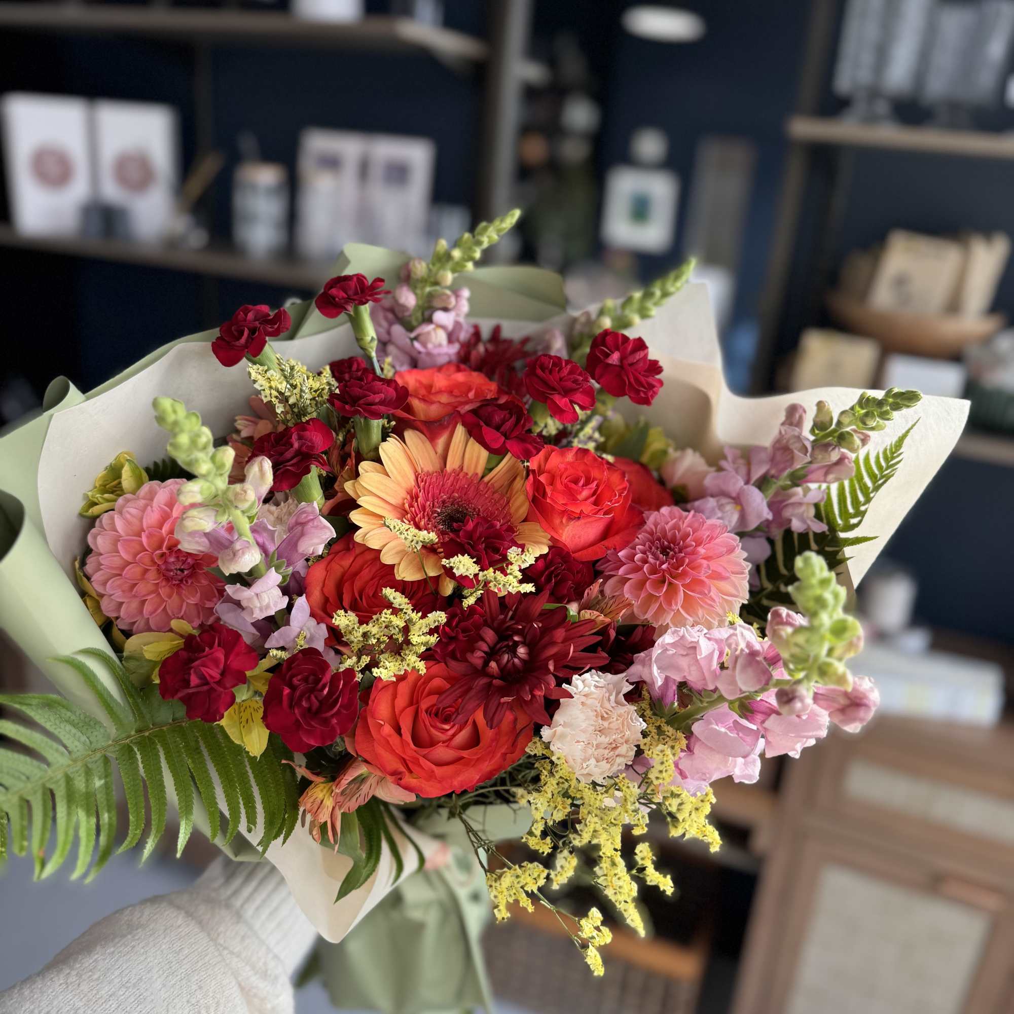 Handheld bouquet of pink, red, and orange flowers wrapped in paper